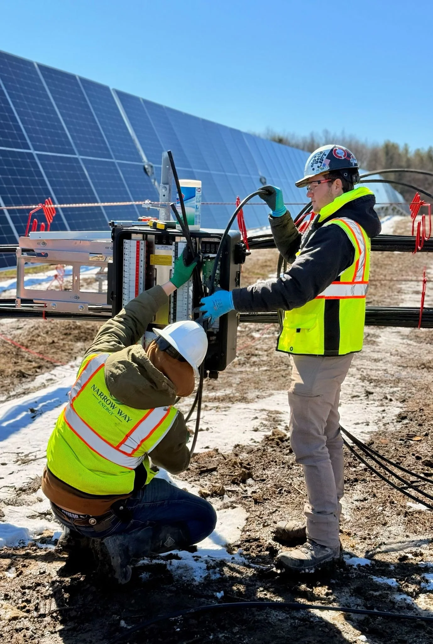 Two workers in safety gear installing or maintaining solar panels outdoors on a partly cloudy day.