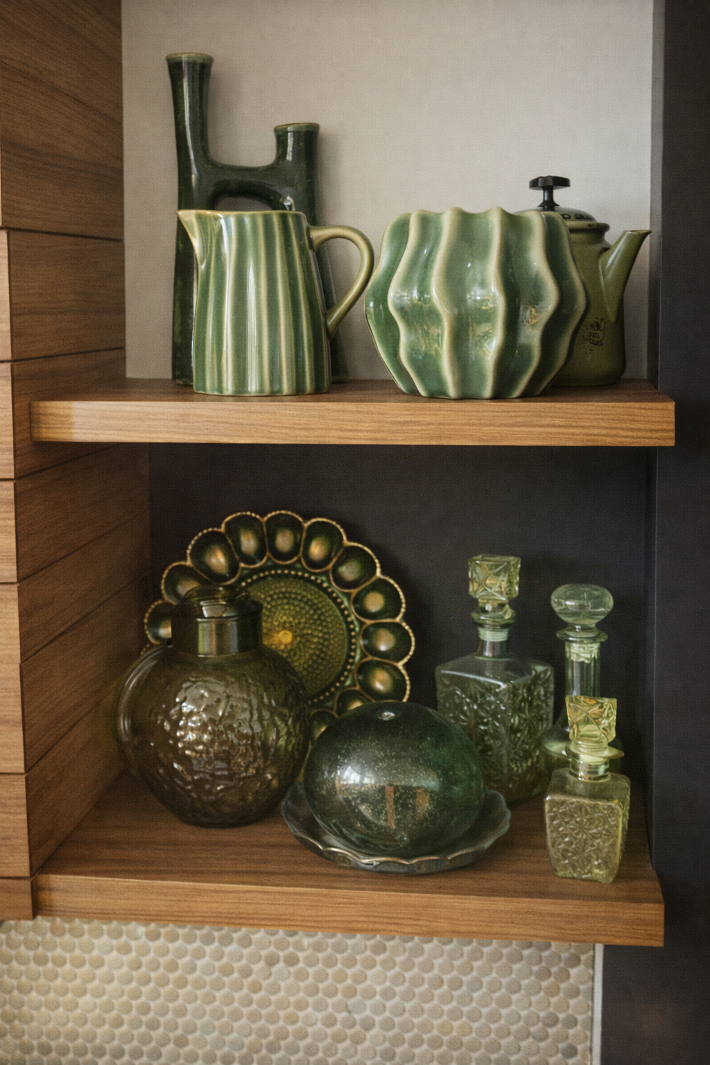 Display of green glassware and ceramic items on wooden shelves, including vases, decanters, and decorative plates.