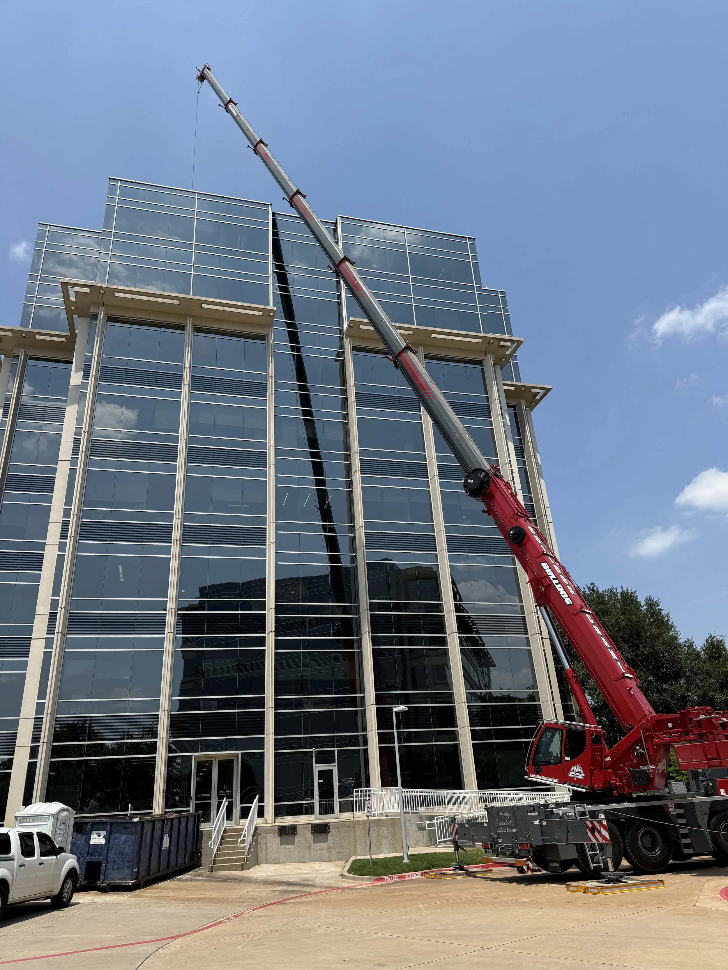 A red crane lifting a tool or material onto the top of a modern glass office building during daytime.