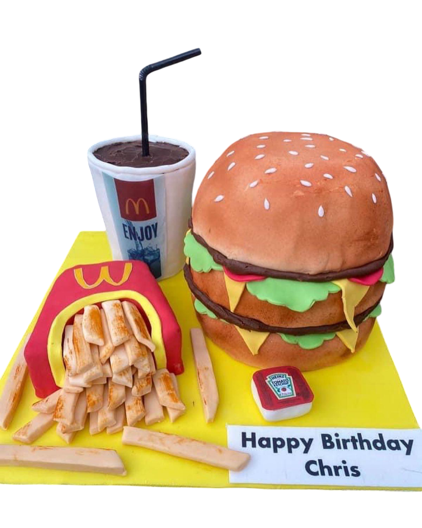 A Burger Cake surrounded by McDonald's-themed food items, including French fry-shaped cookies and a soda cup with a straw. The cake and treats are on a yellow birthday cake board with a birthday message for Chris.