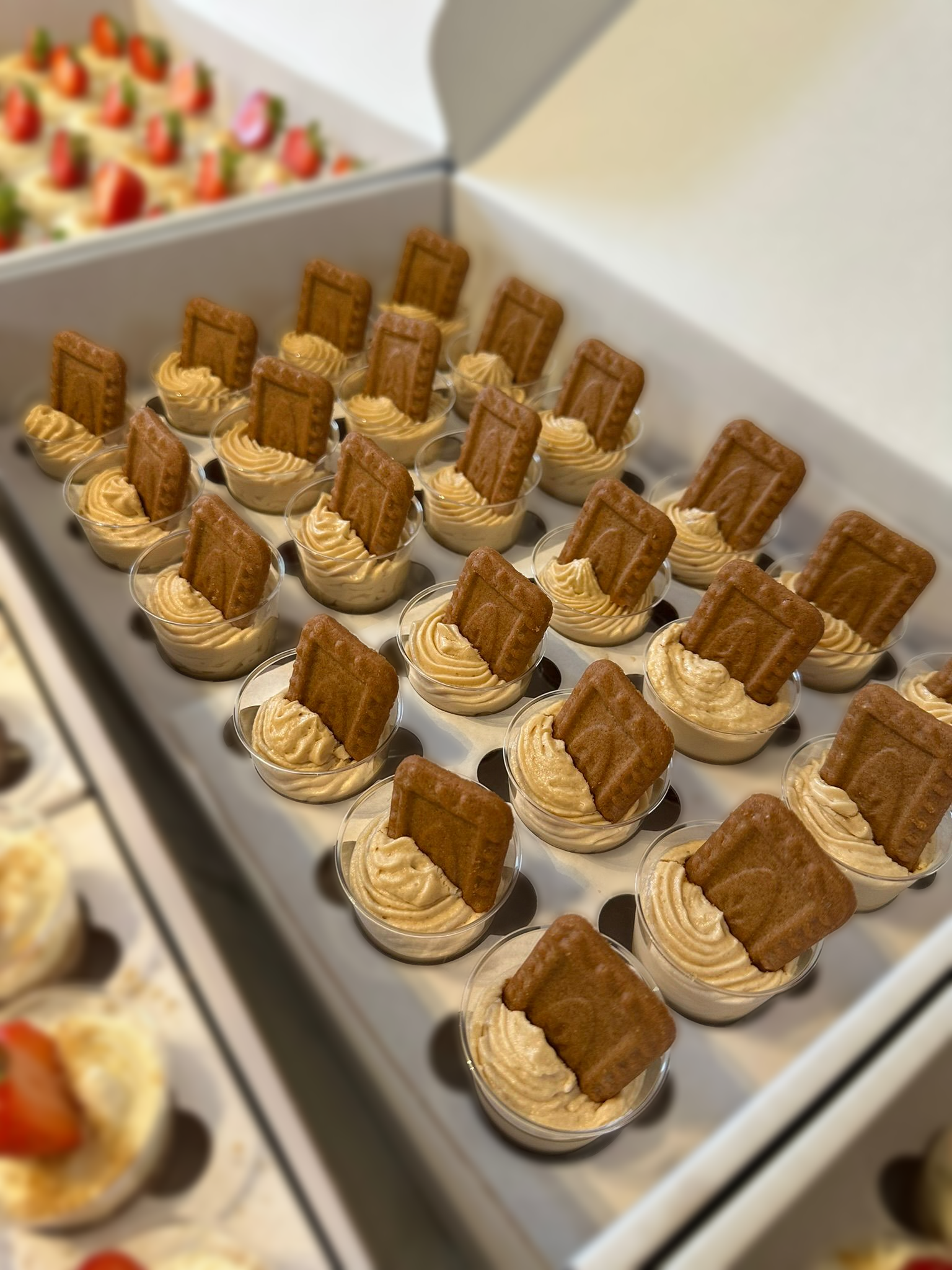 Dessert cups with piped cream and a rectangular cookie on top, arranged in rows in a white display box.