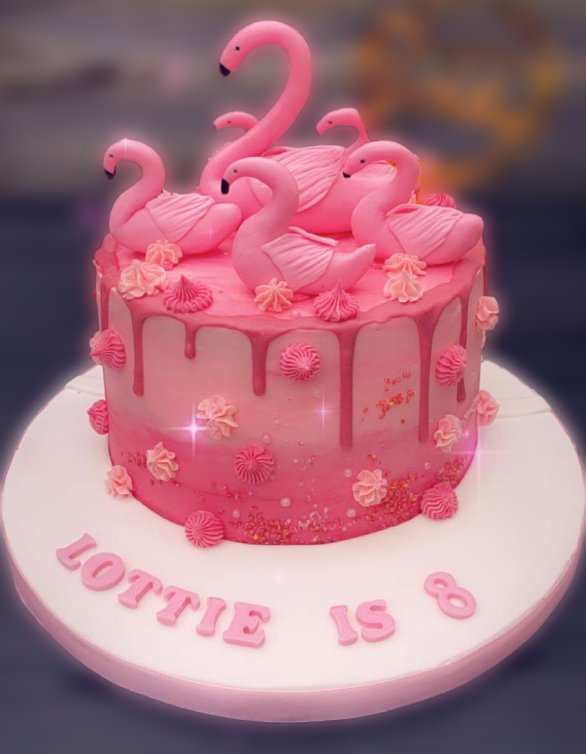 Pink celebration cake with five flamingo decorations on top, pink fondant drips, and pink icing accents, on a white cake board that says 'LOUIE 15 8'.