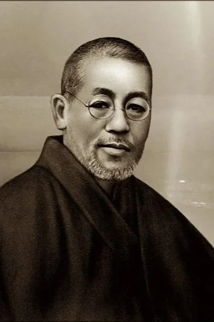 Portrait of a man with glasses, short hair, and a beard, wearing traditional Japanese clothing, against a plain background.