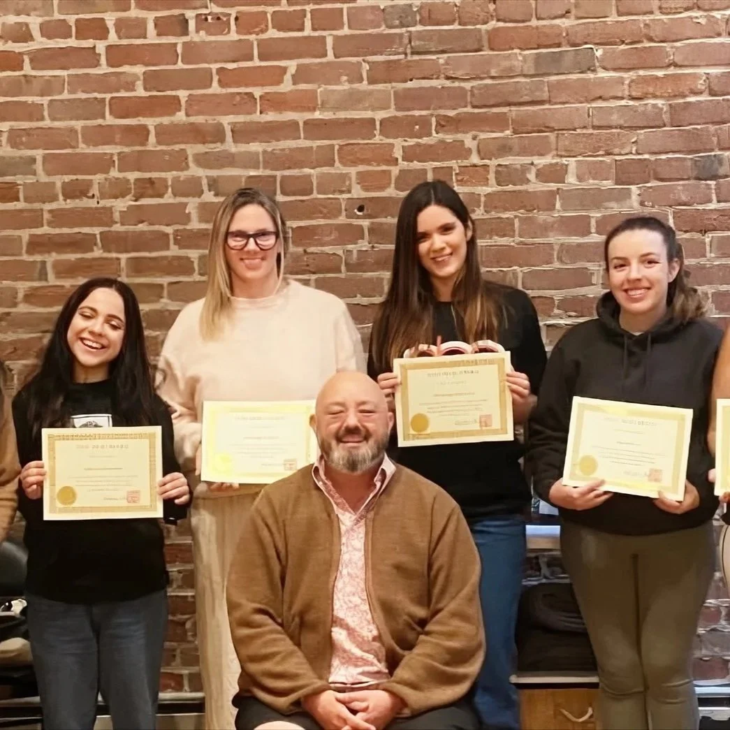 Four women standing behind a seated man, each holding a certificate, in front of a brick wall.