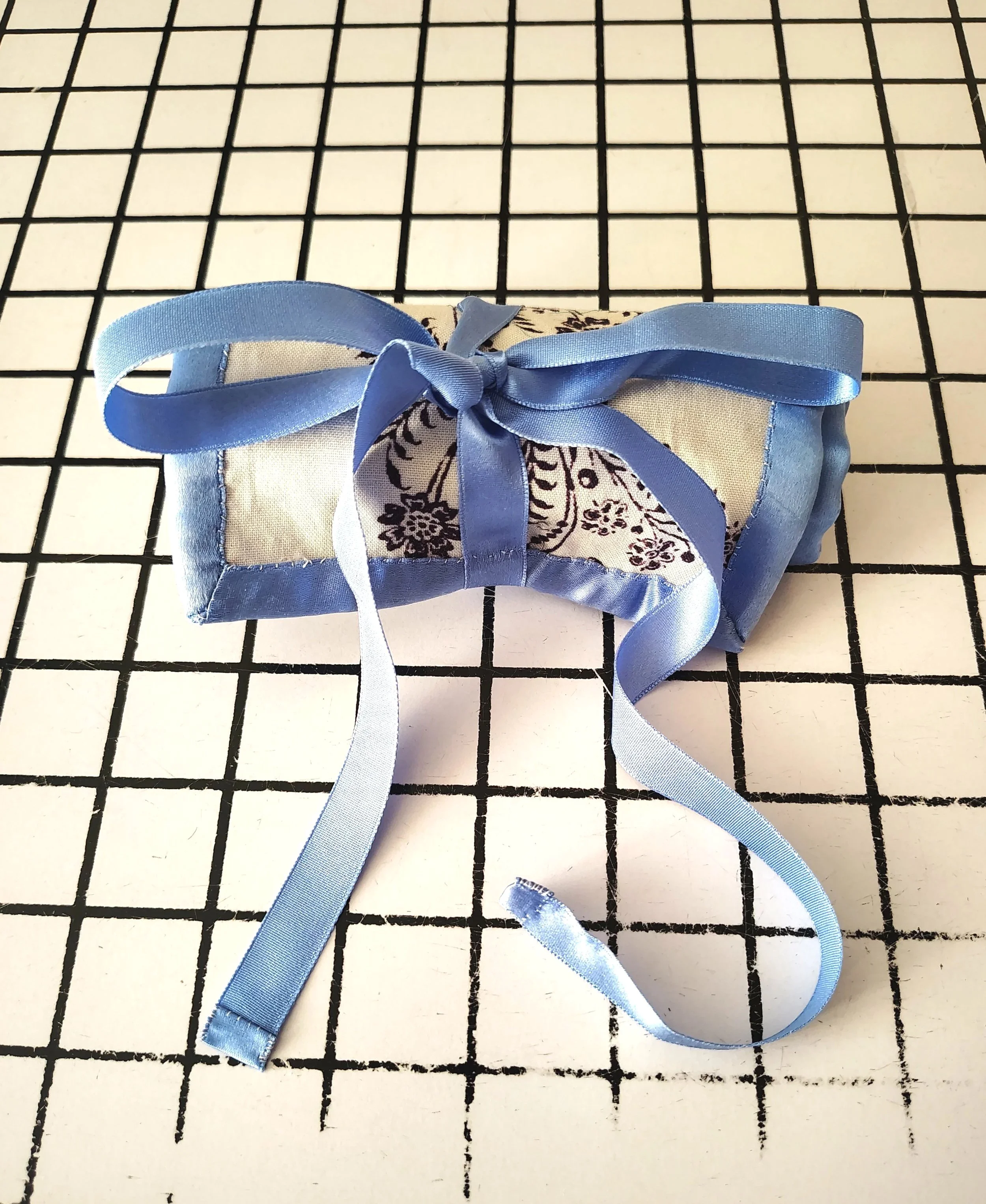 A fabric sachet decorated with a blue satin ribbon, sitting on a black and white grid-patterned surface.