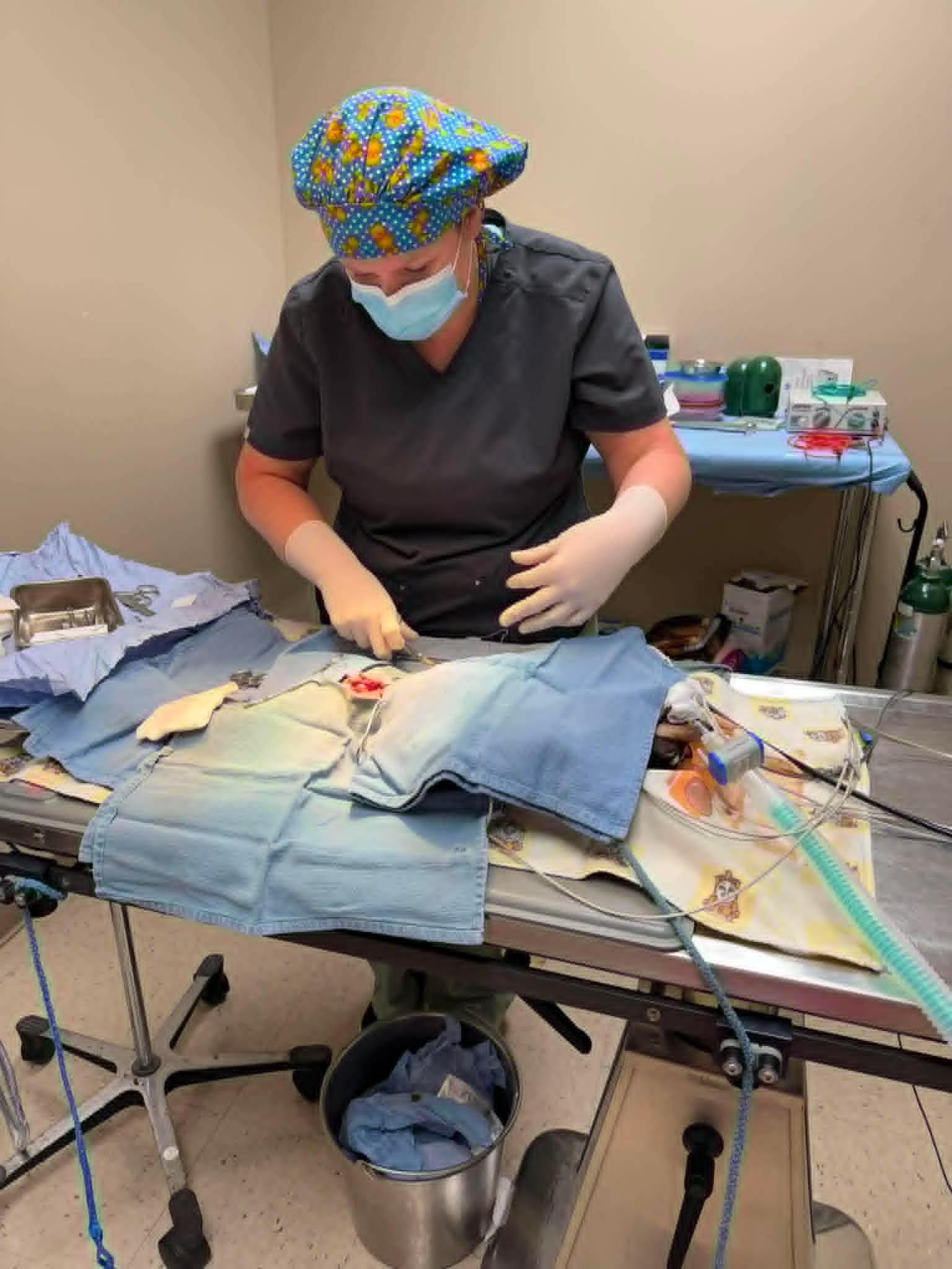 Medical professional wearing scrubs, a colorful surgical cap, and a mask, preparing a patient for surgery in an operating room with surgical instruments and equipment.