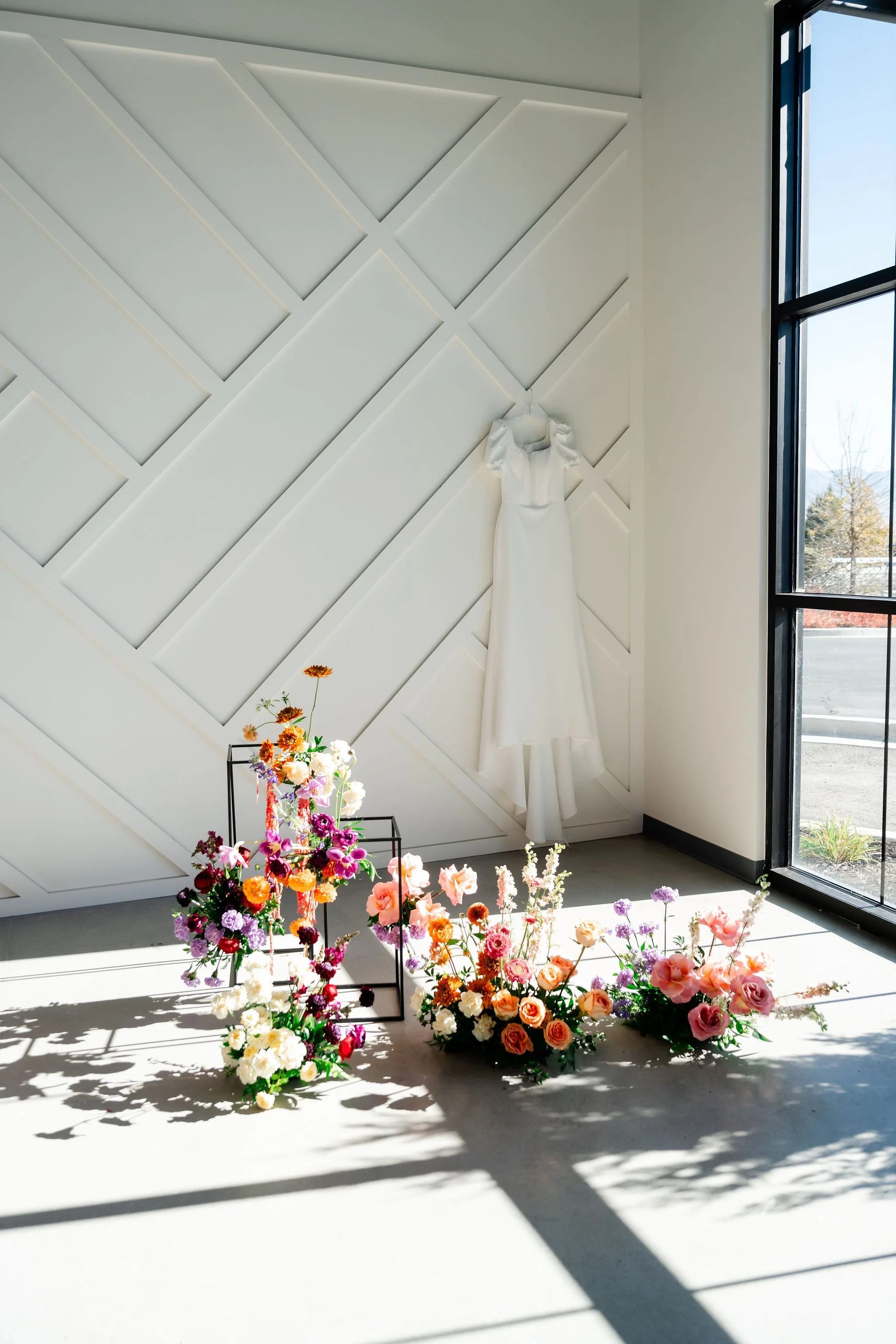 Our wainscoting wall with a white wedding gown hung on it and a beautiful bright floral arrangement in front of it