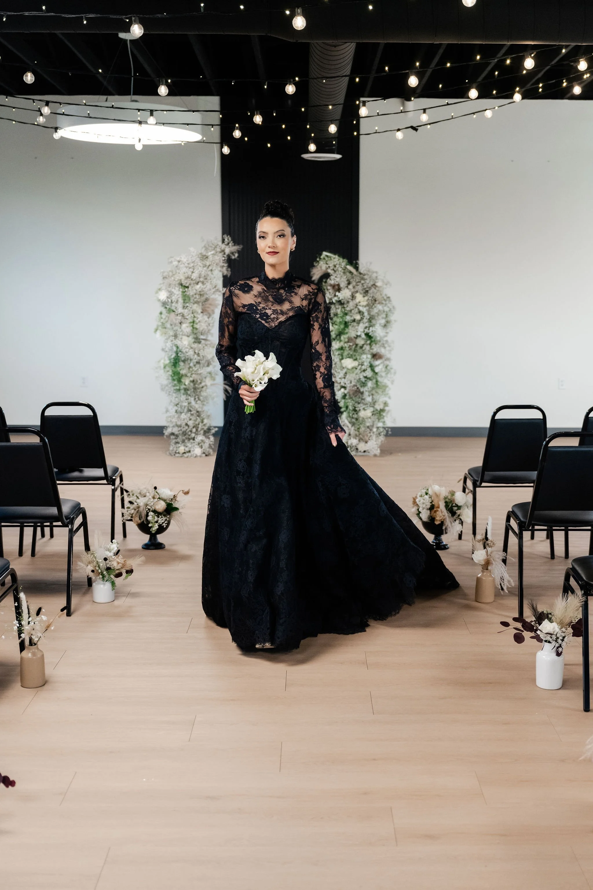 A bride in a black wedding gown coming down the aisle of a ceremony setup in our Starlight loft