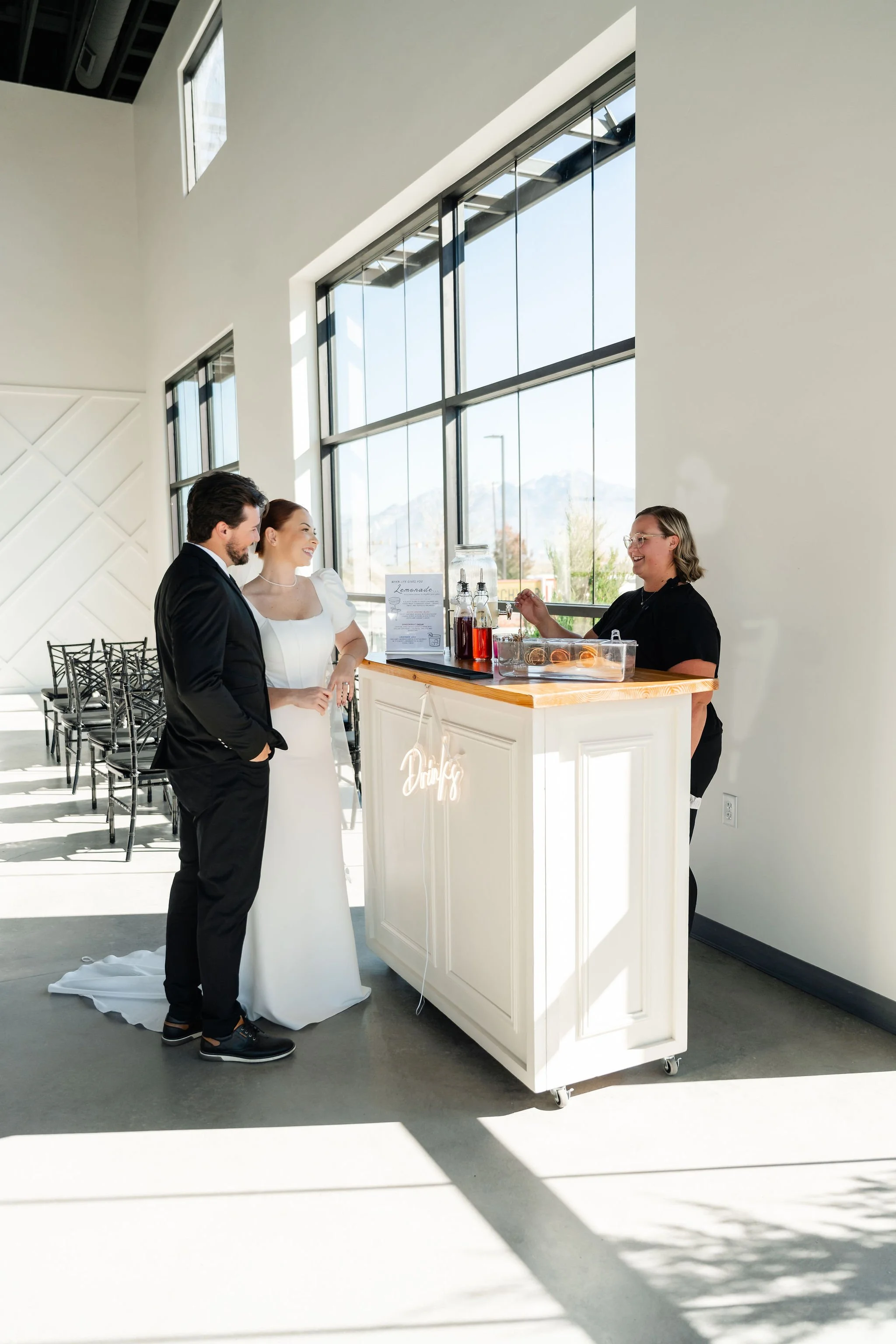 Bride and groom grab a couple drinks from a white bar setup in our spacious Enchanted Hall