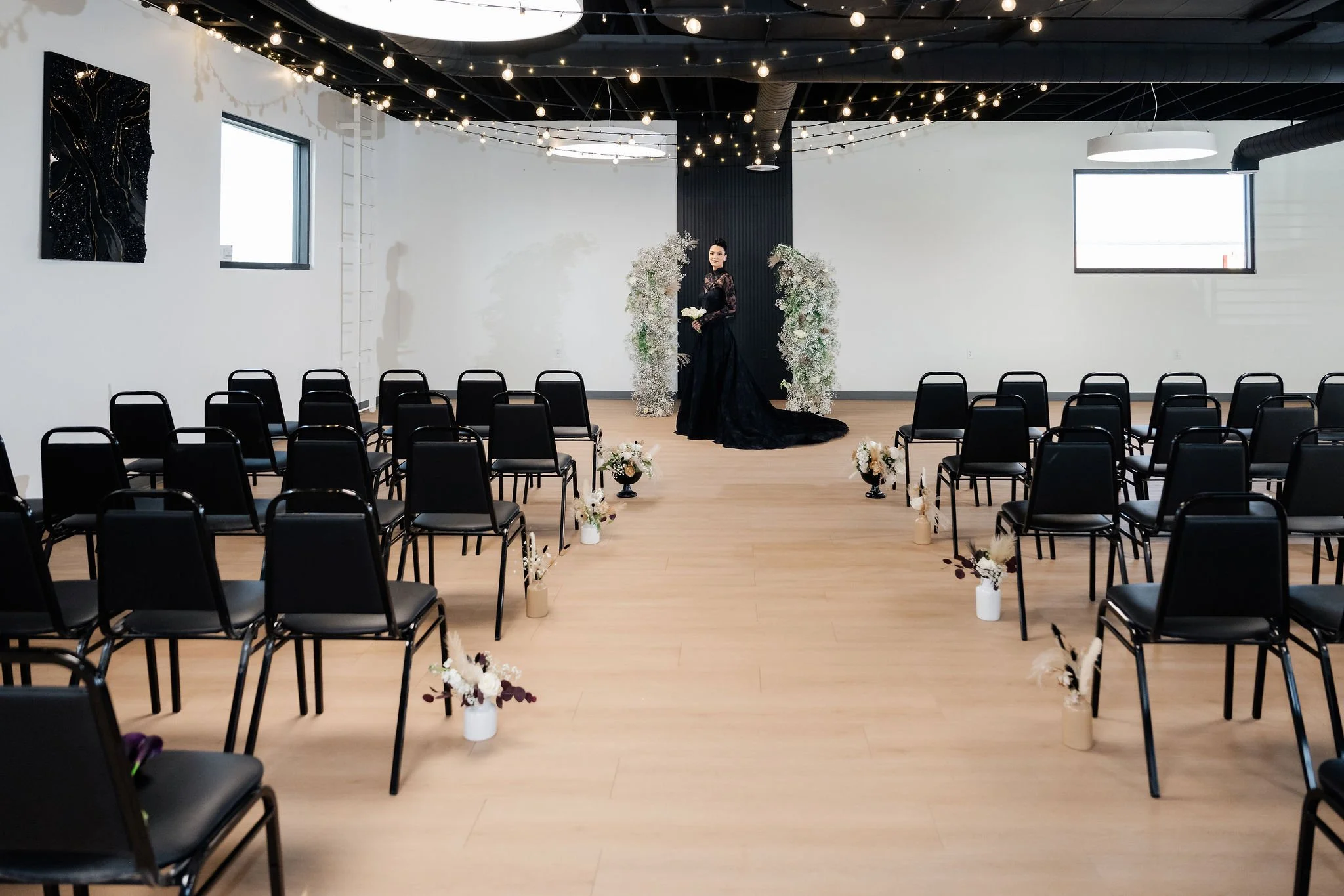 Our Starlight Loft setup with ceremony seating with a floral centerpiece and a bridge in a black wedding gown and string lights hung above