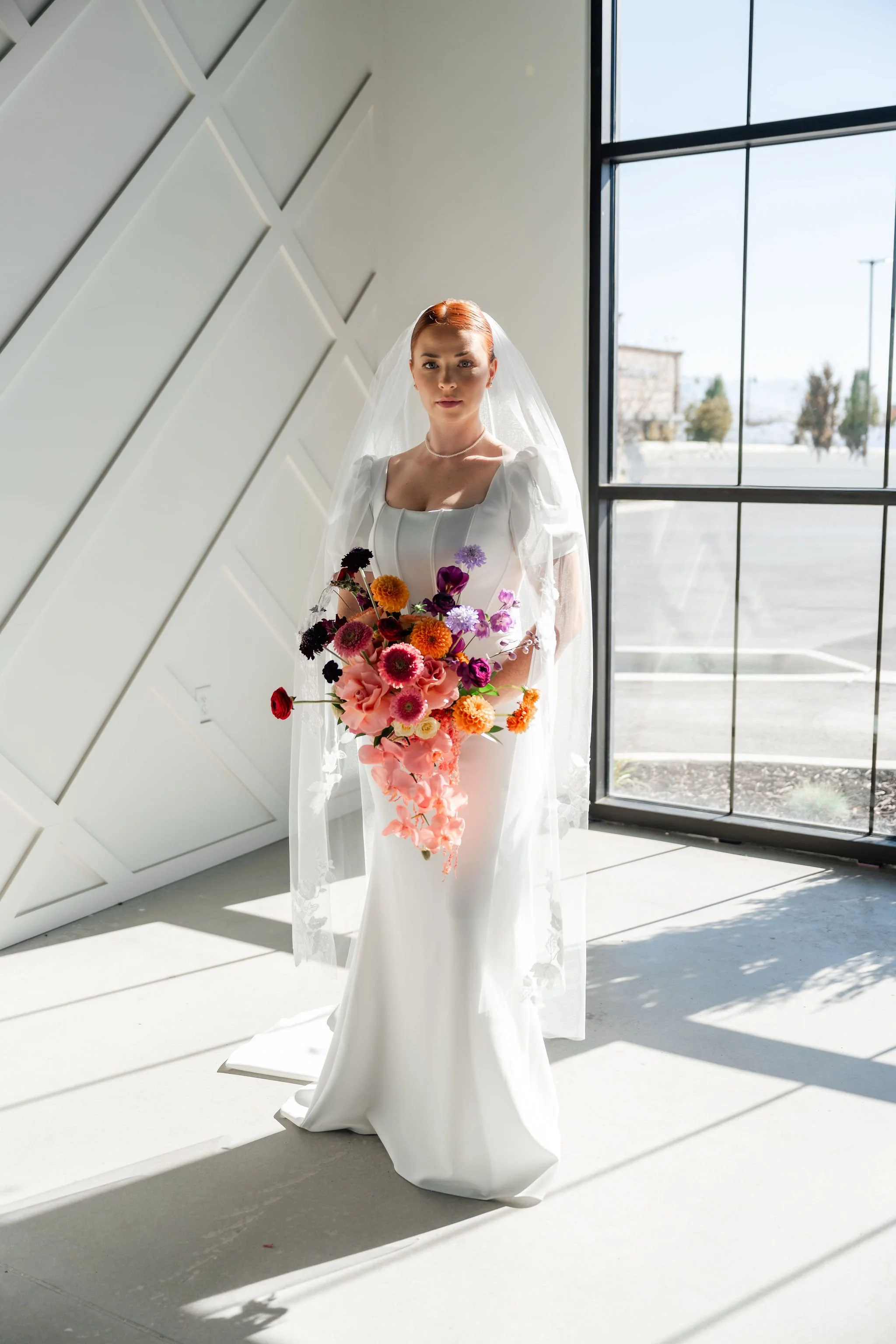 Bride in a white wedding dress with a colorful and lush bouquet stands in the corner of our Enchanted Hall