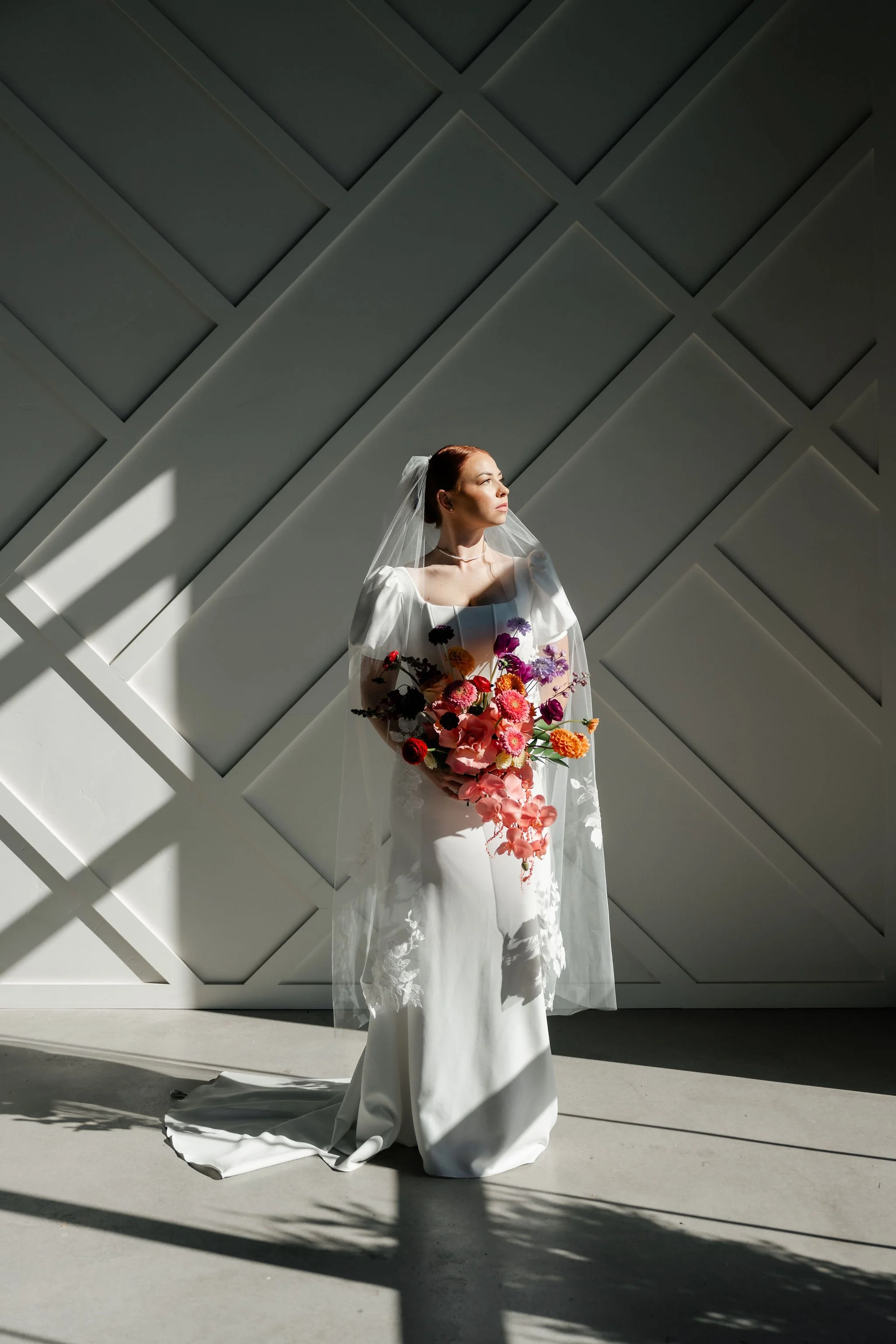 Bride in a white wedding dress with a colorful and lush bouquet stands in front of our wainscoting wall in our Enchanted Hall