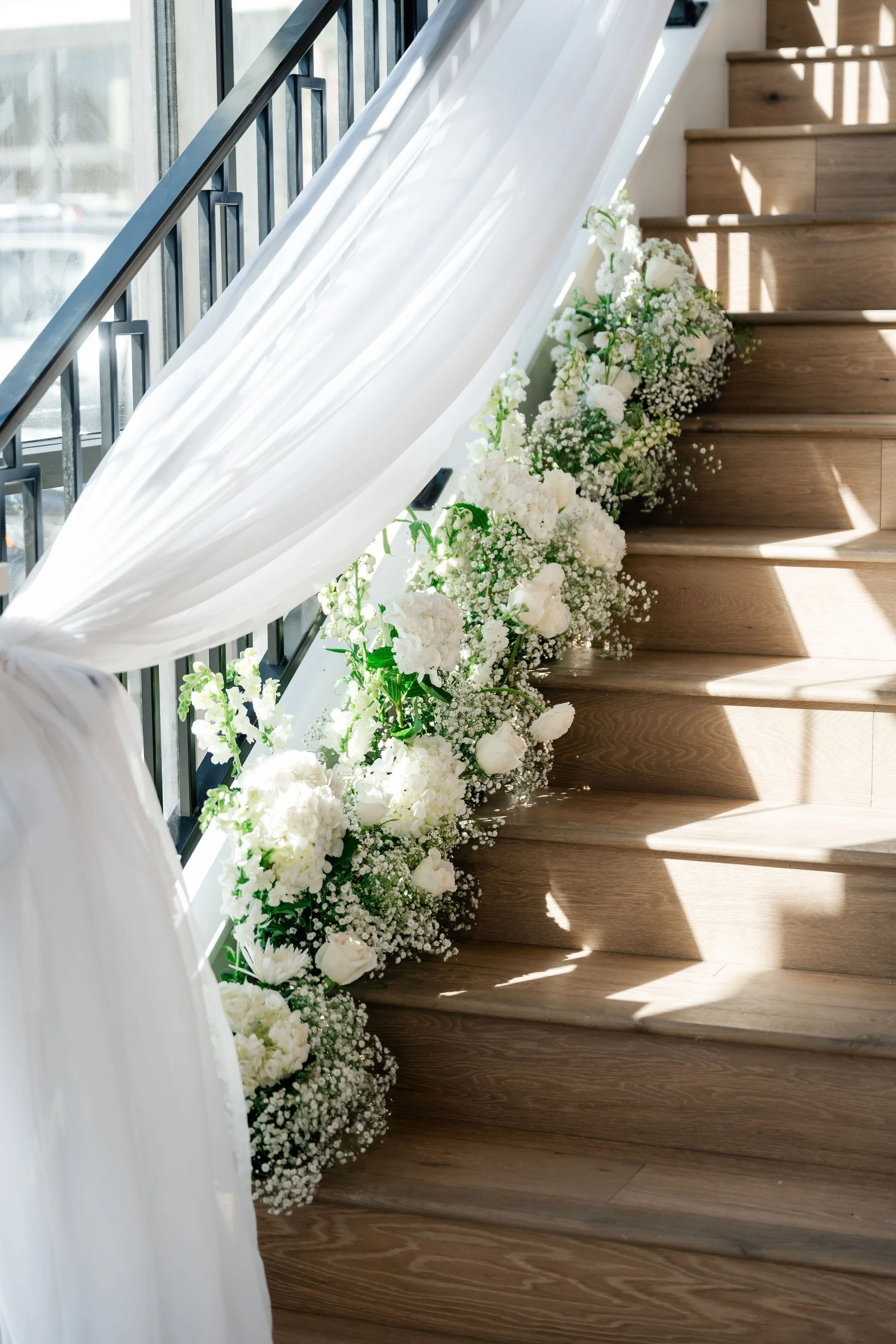 Closeup view of wooden staircase with elegant white floral arrangements and drapery