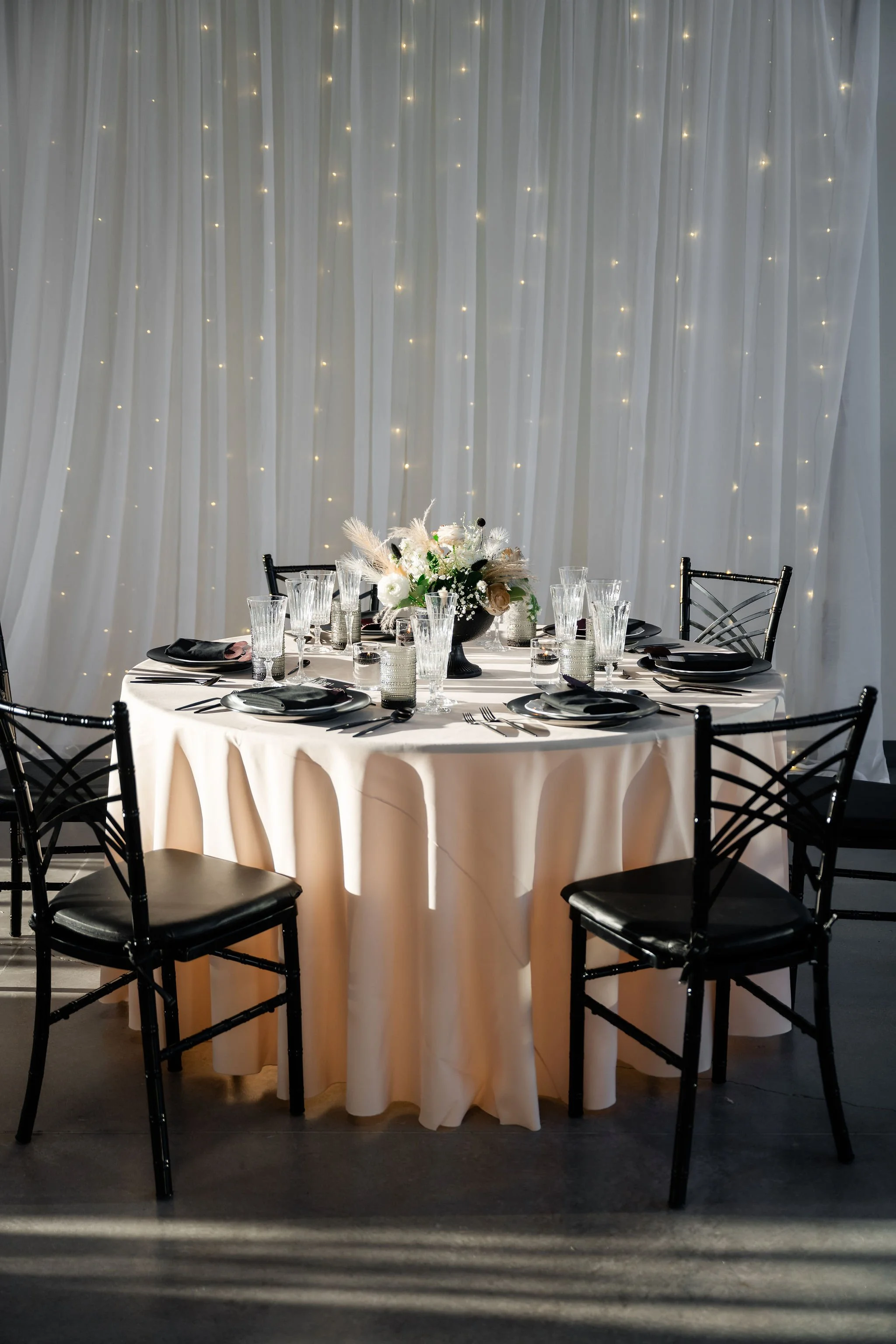A round dining setup with a white draped and lit backdrop in our Enchanted Hall