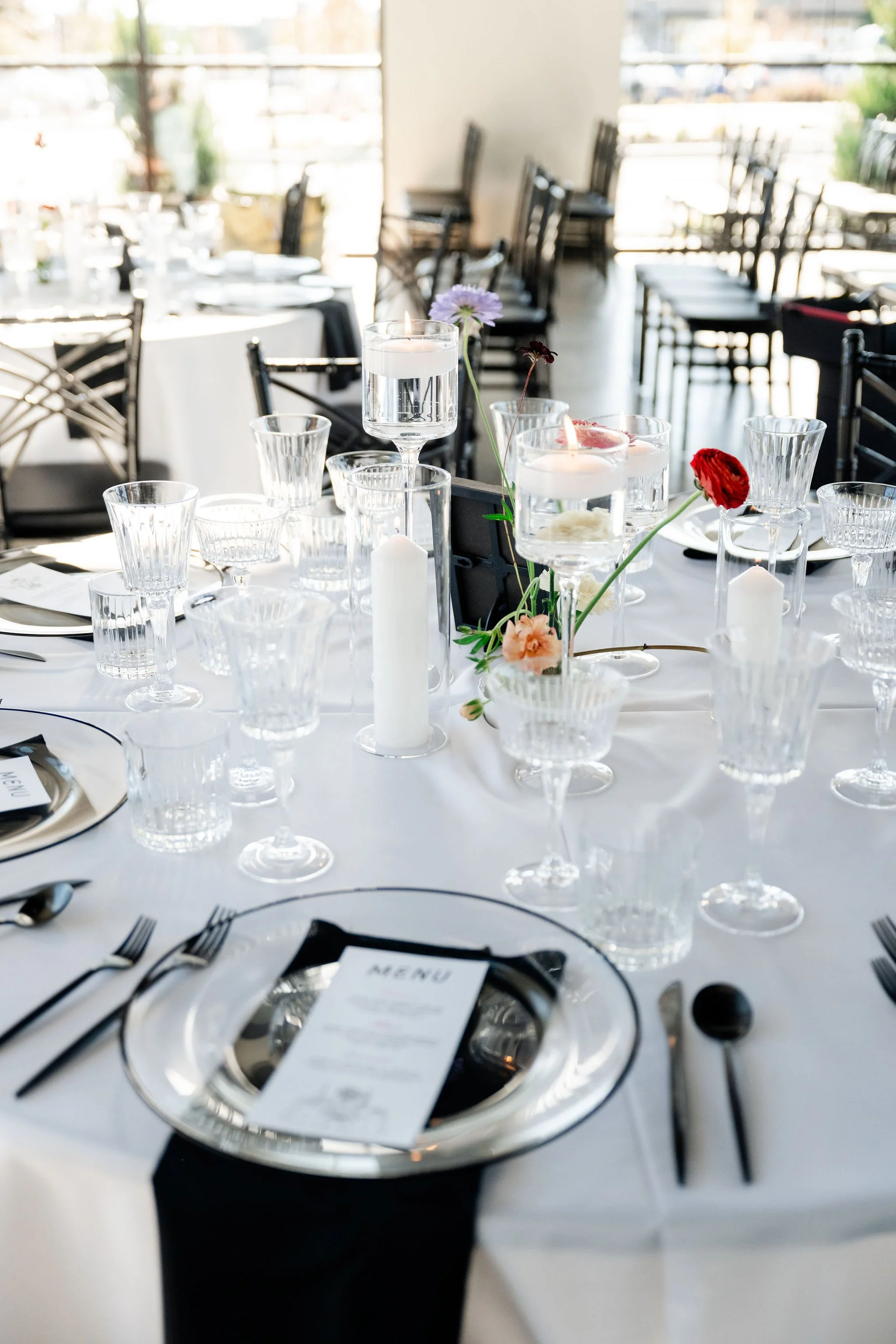 Dining setup with black utensils, glass plates, and floral centerpieces with an audience seating background