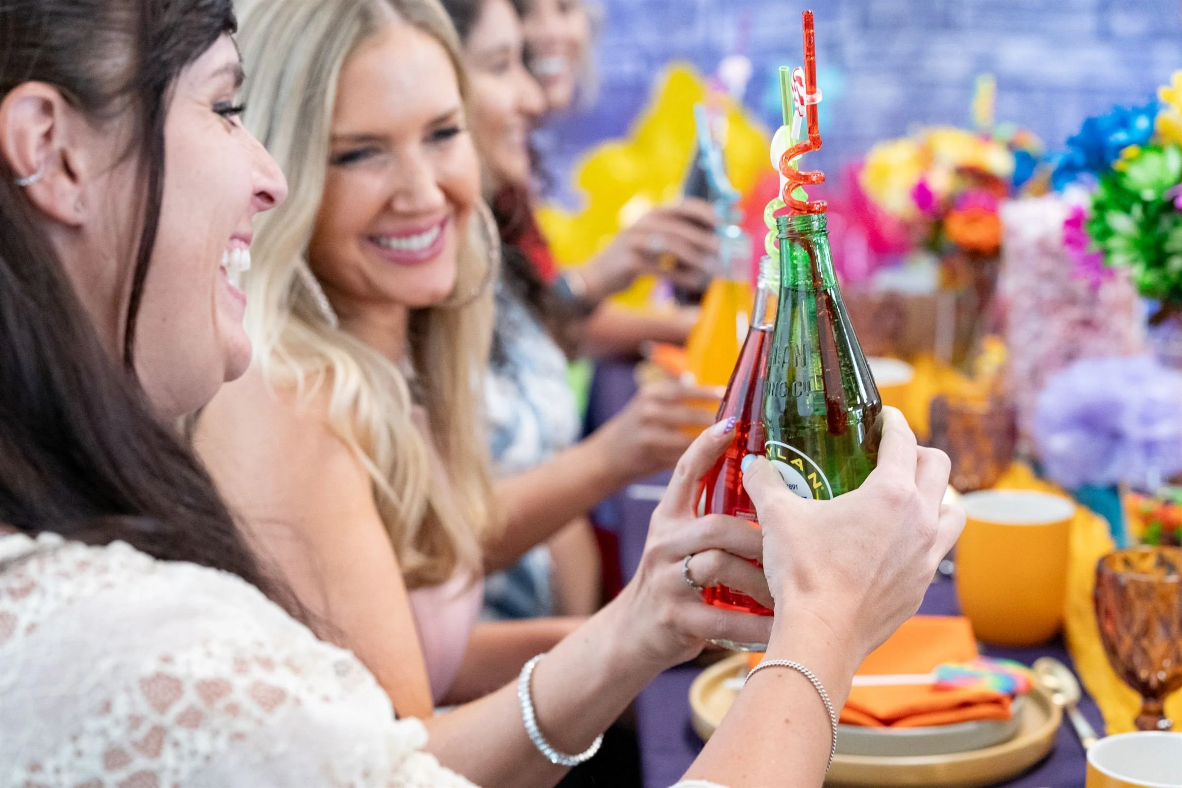 Friends toast colorful glasses and crazy straws in Herriman event center