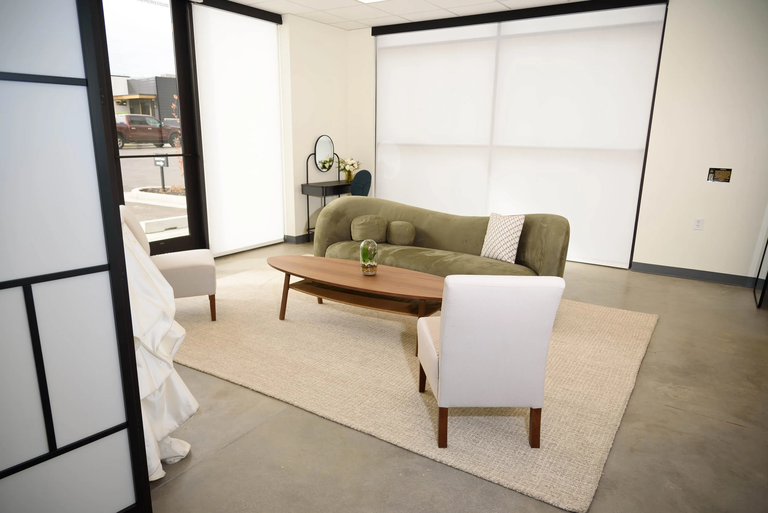 A white wedding gown peeks out from a privacy screen in our getting ready room with our elegant modern green couch, beige chairs, and vanities