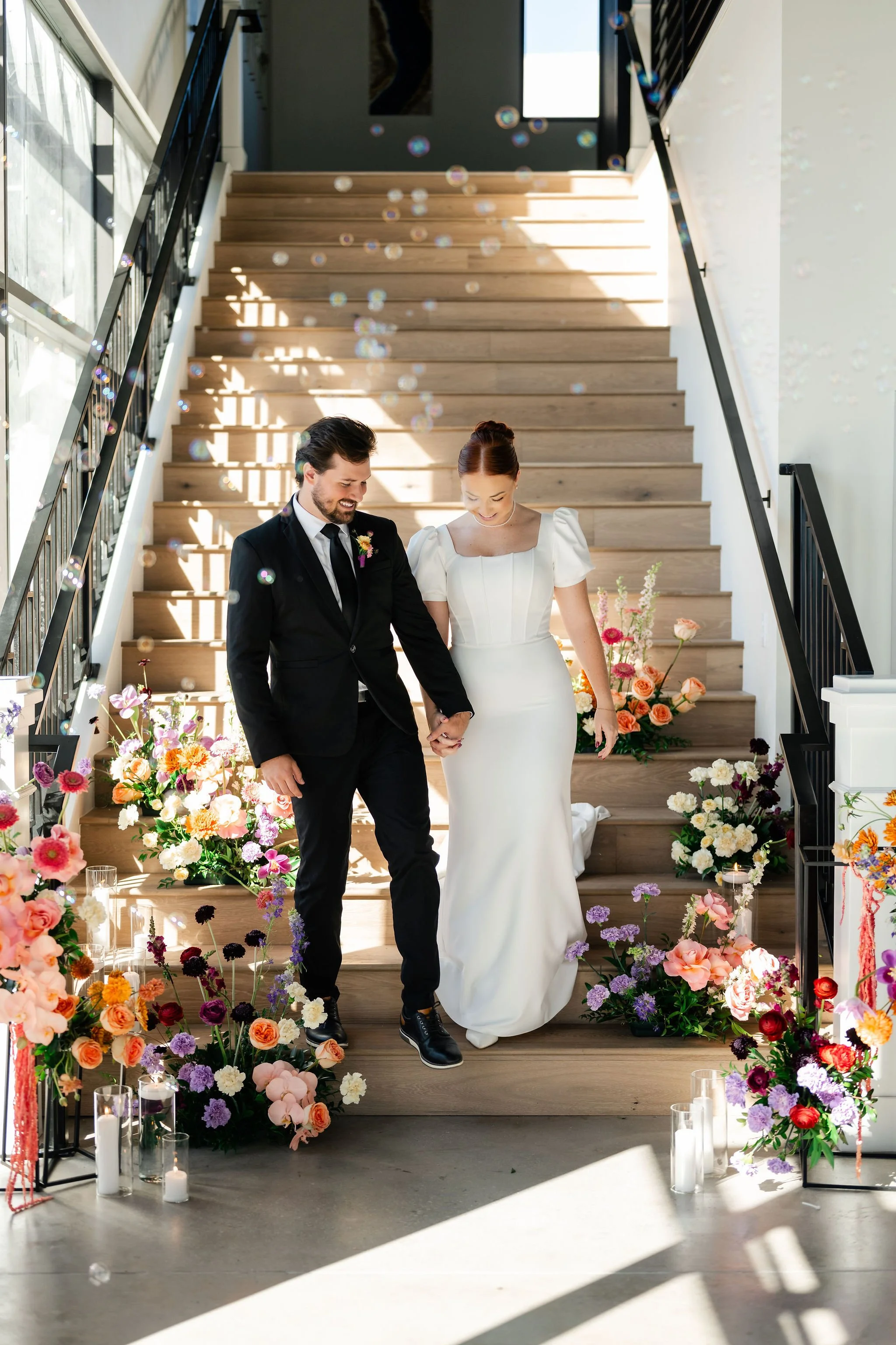 Bride and groom in traditional black tux and white wedding gown showcasing our luxurious staircase elevated with colorful floral arrangements