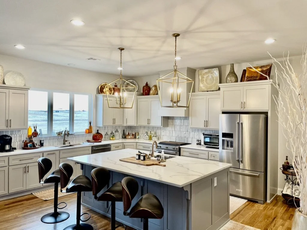 Modern white kitchen with island, stainless steel refrigerator, and decorative vases and artwork on top of cabinets.