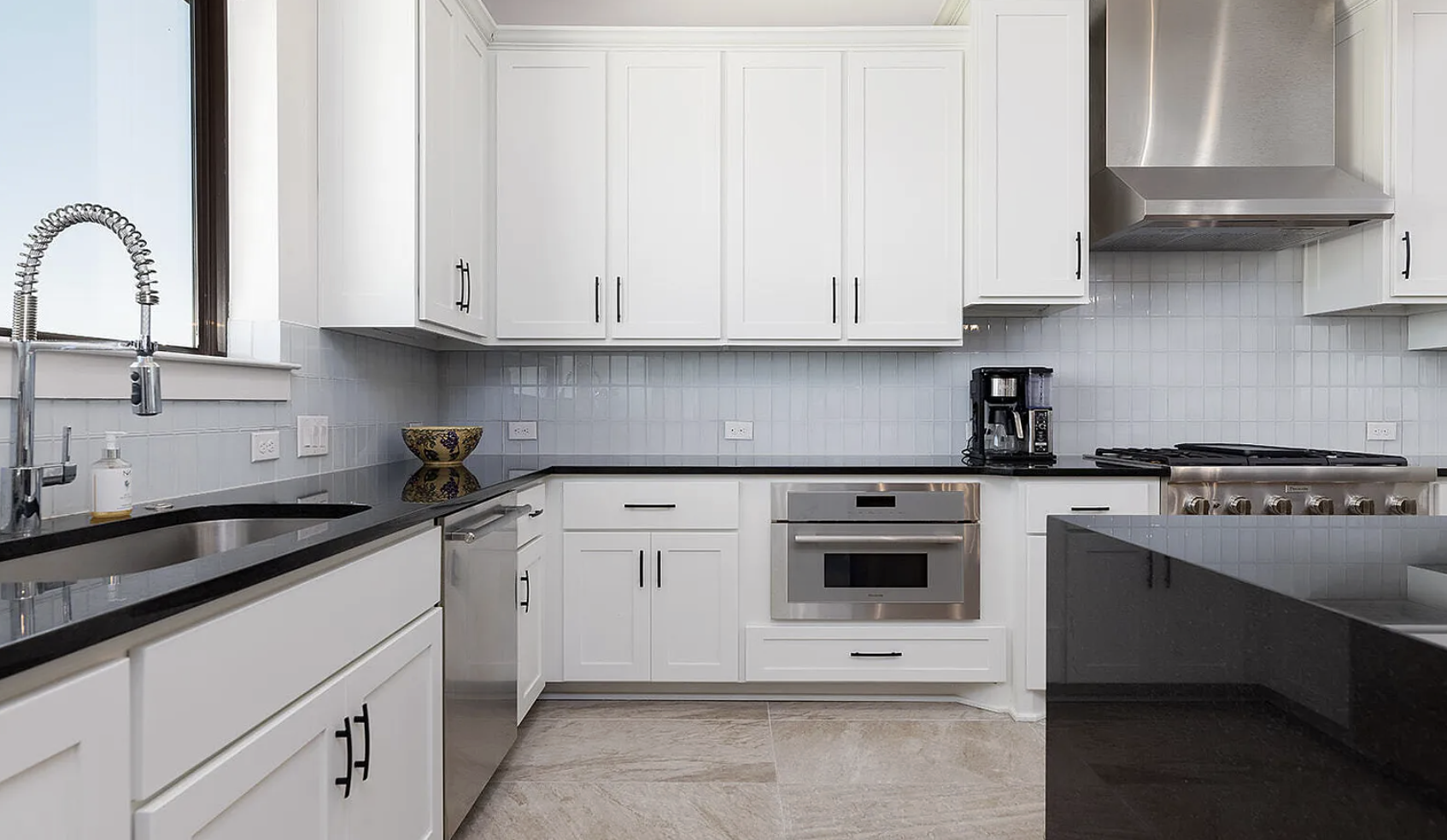Modern kitchen with white cabinets, black countertops, stainless steel appliances, and a window above the sink.