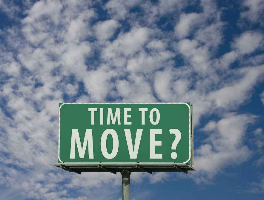 Green highway sign that reads "Time to Move?" against a blue sky with scattered clouds.