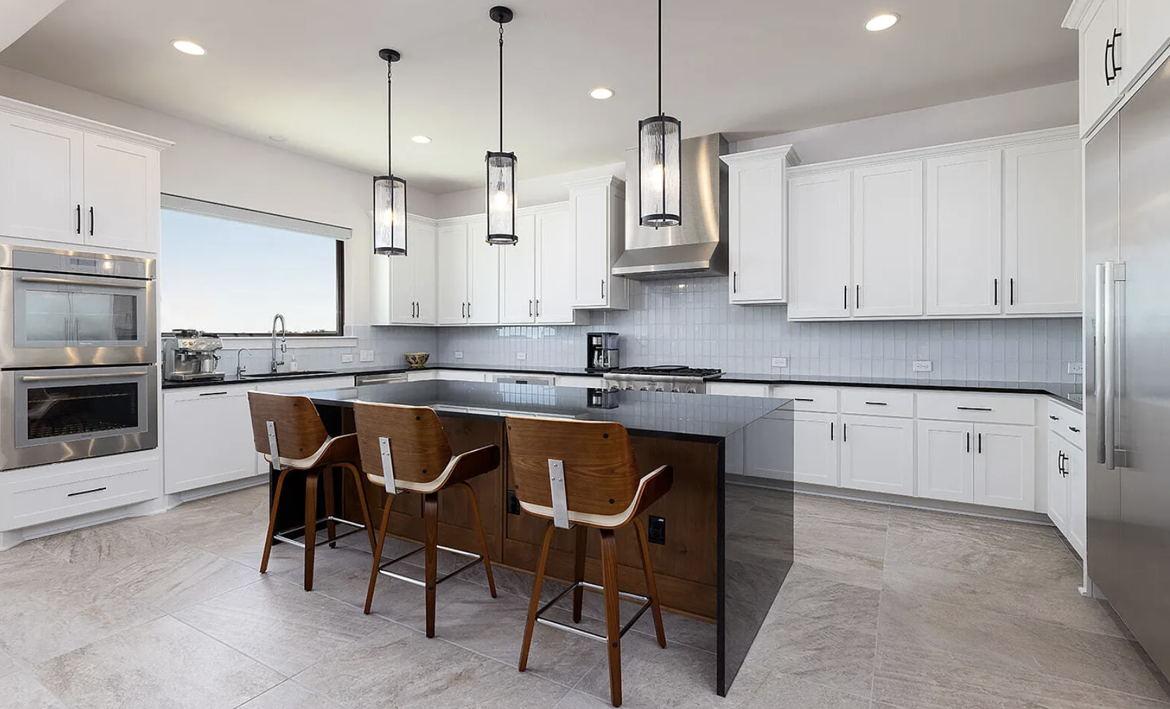 Modern kitchen with white cabinets, black countertops, a large window, and a center island with three wooden chairs.