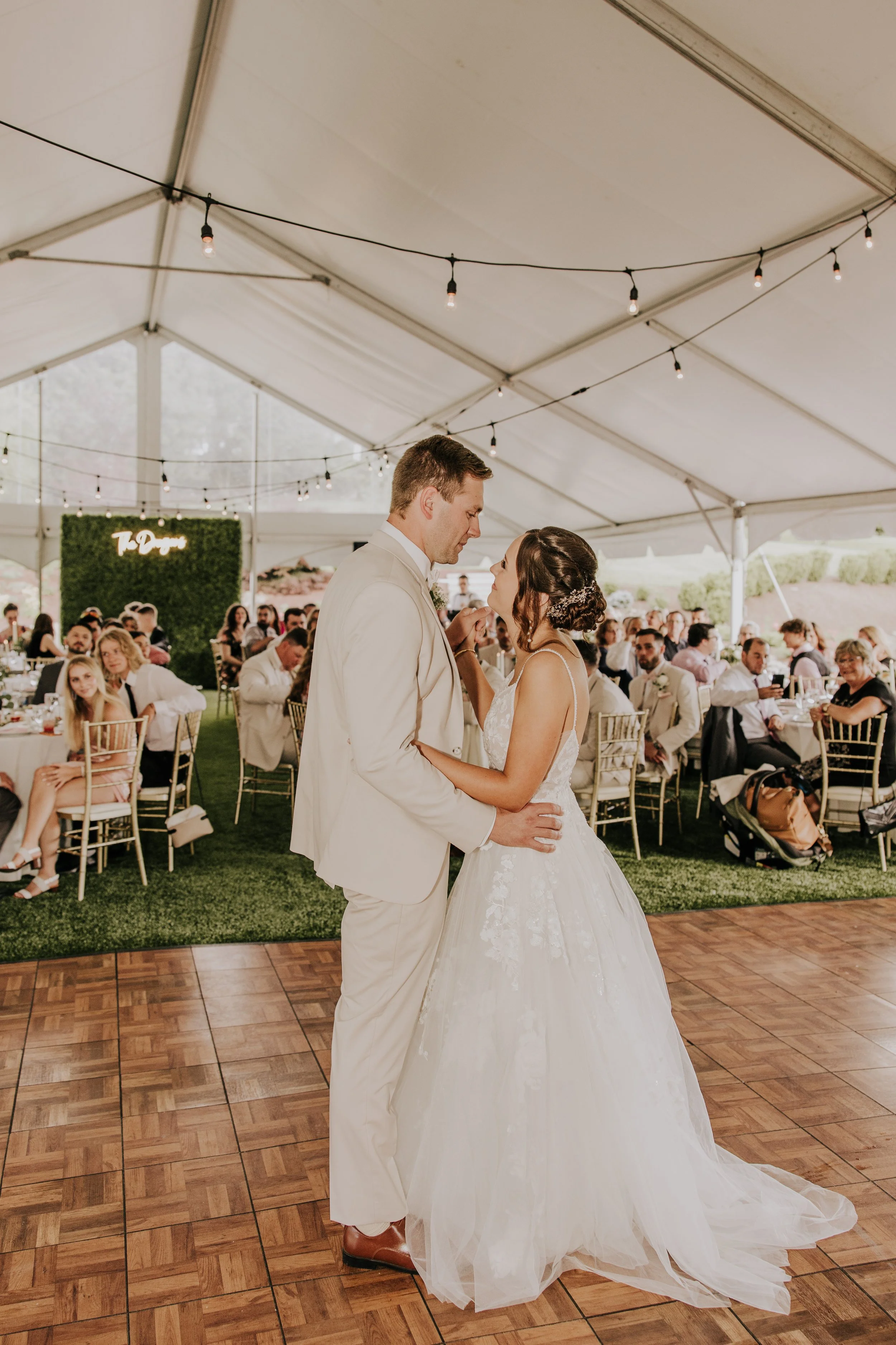 A bride and groom sharing their first dance at a wedding reception inside a tent with guests seated at tables.