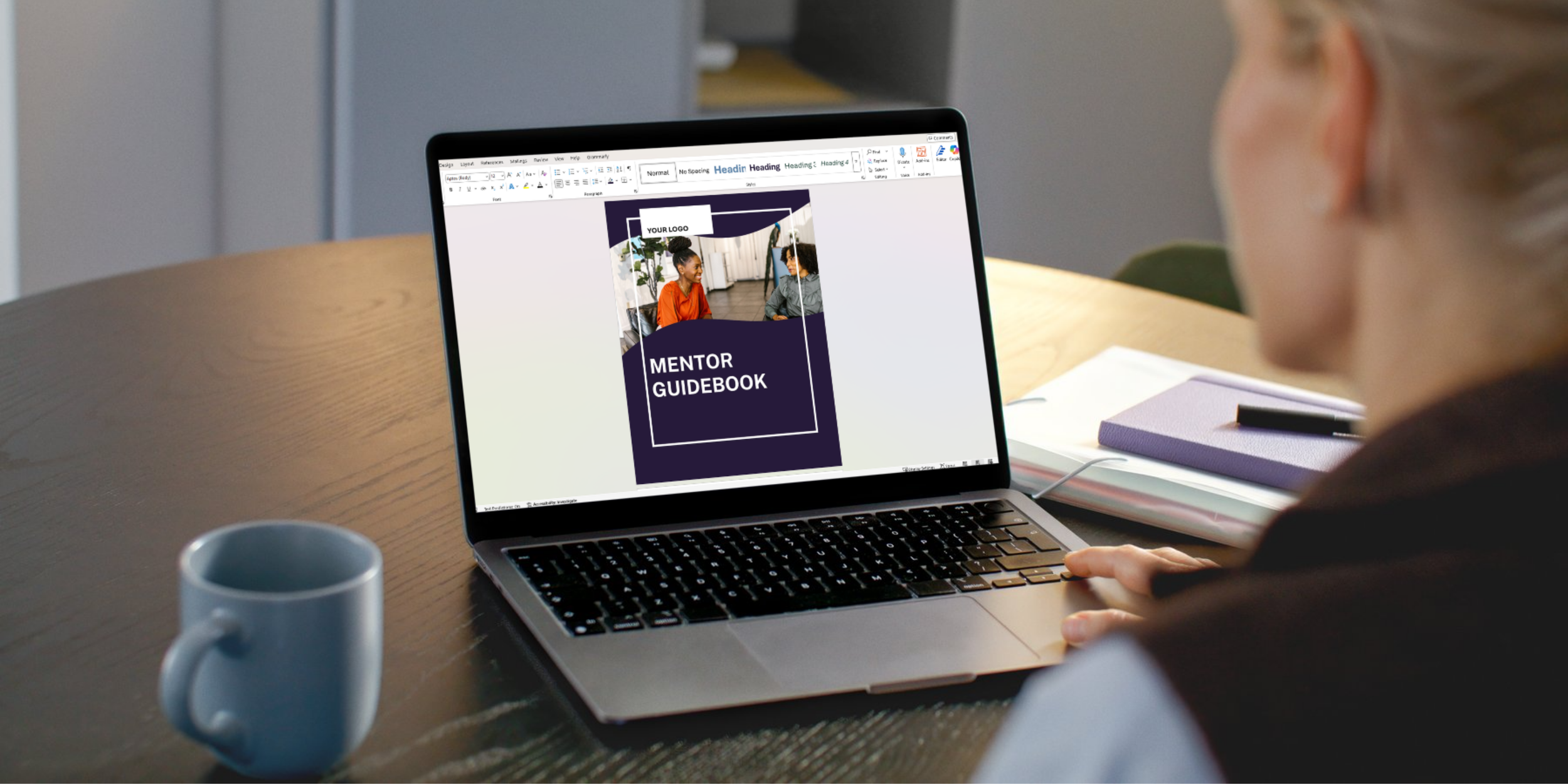 A person working on a laptop at a desk, viewing a guidebook titled "Mentor Guidebook" with a picture of two women talking.