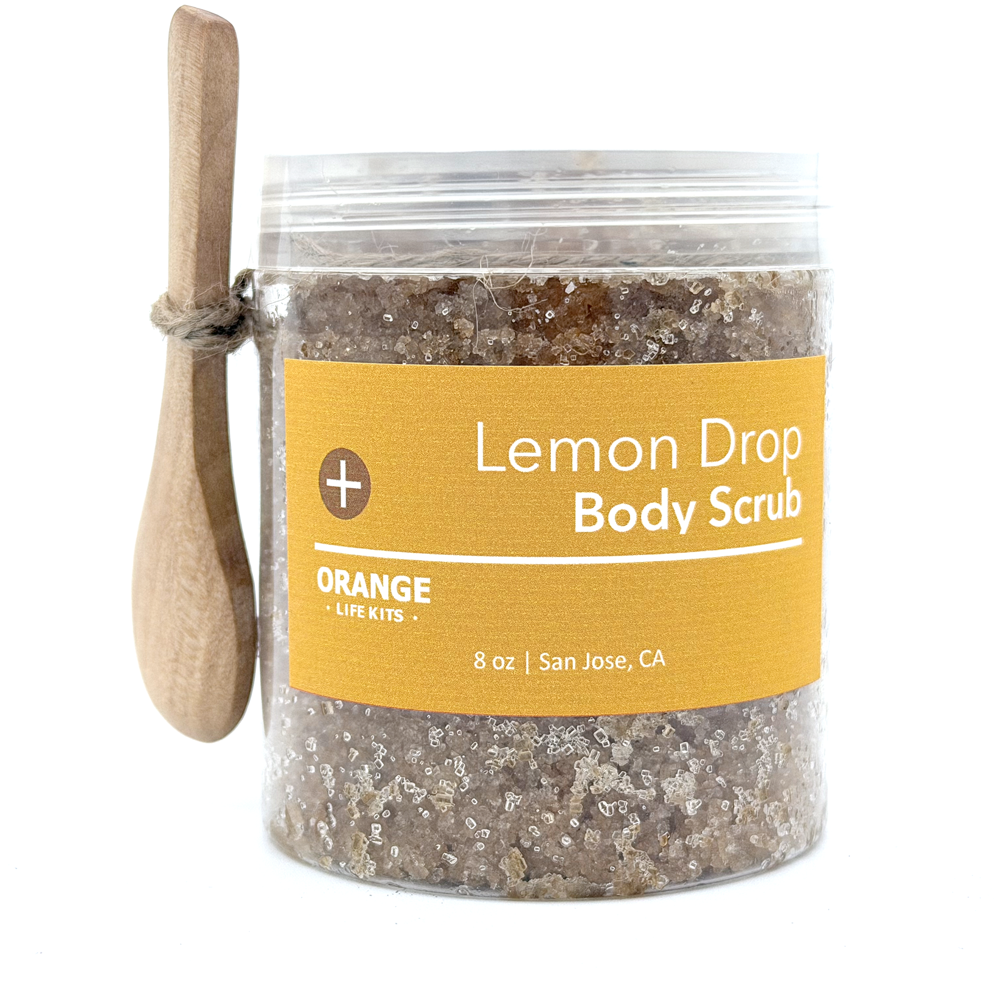 A container of lemon drop body scrub with a wooden spoon leaning against it.