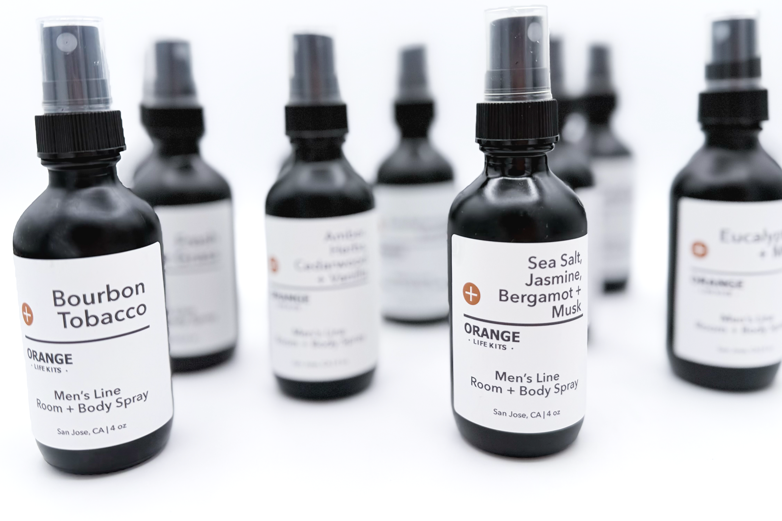 Several black spray bottles with white labels, containing scented room and body spray, arranged in a staggered formation.