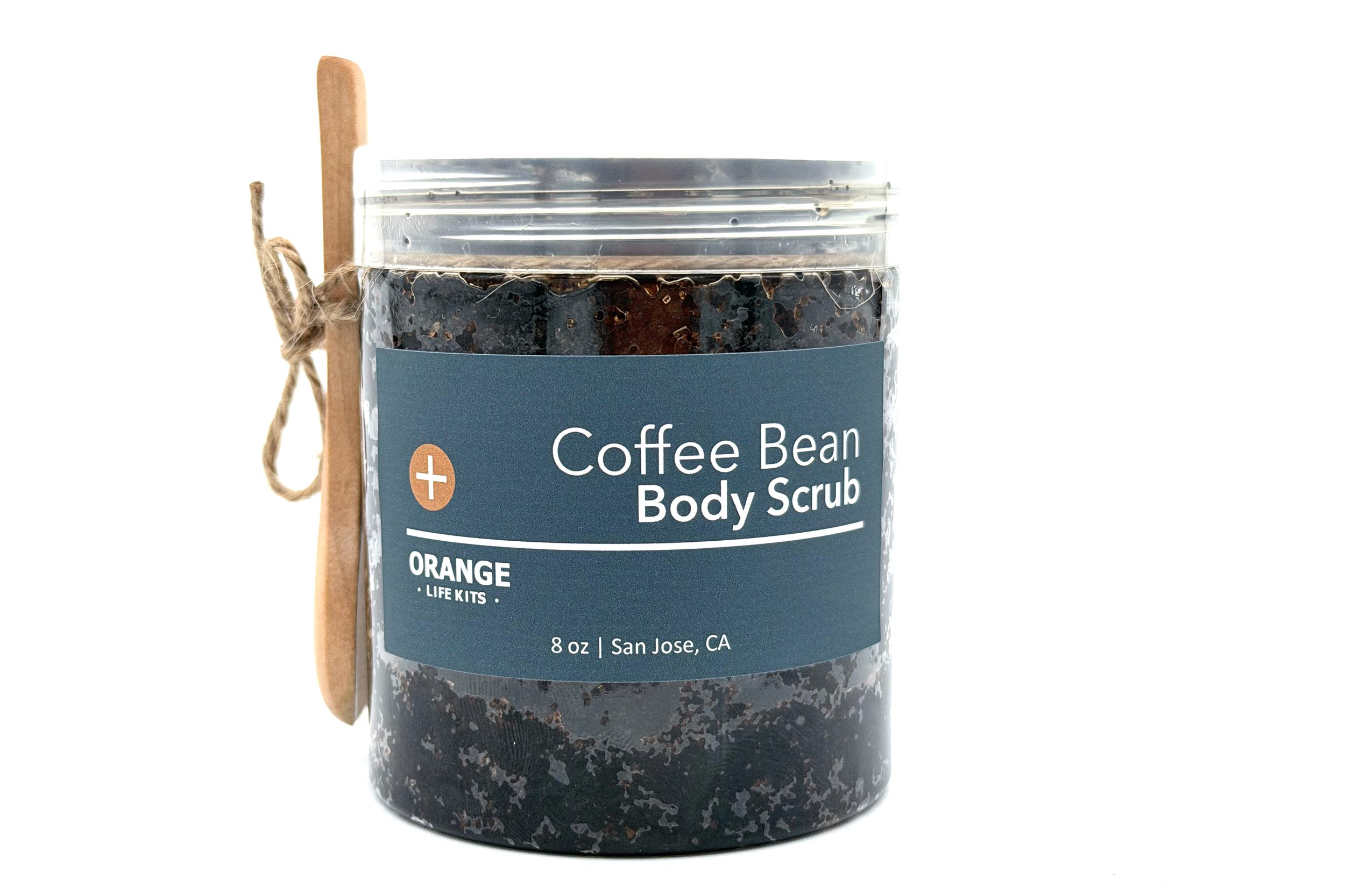A jar of coffee bean body scrub with a wooden spoon and twine tied to the lid, labeled as orange scent, 8 ounces, from San Jose, California.
