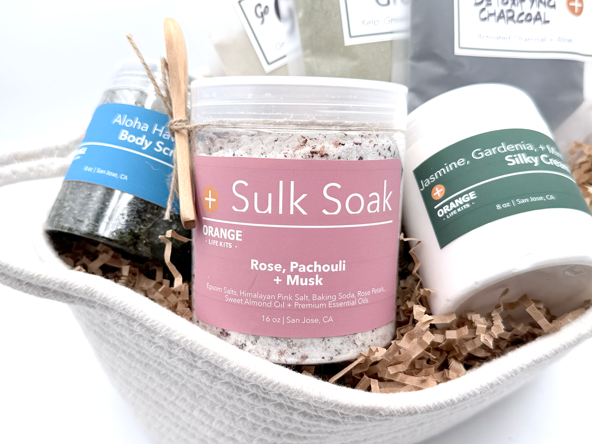 A gift box contains labeled skincare products, including a body scrub, a herbal soak, and a silky cream, surrounded by crinkle paper.