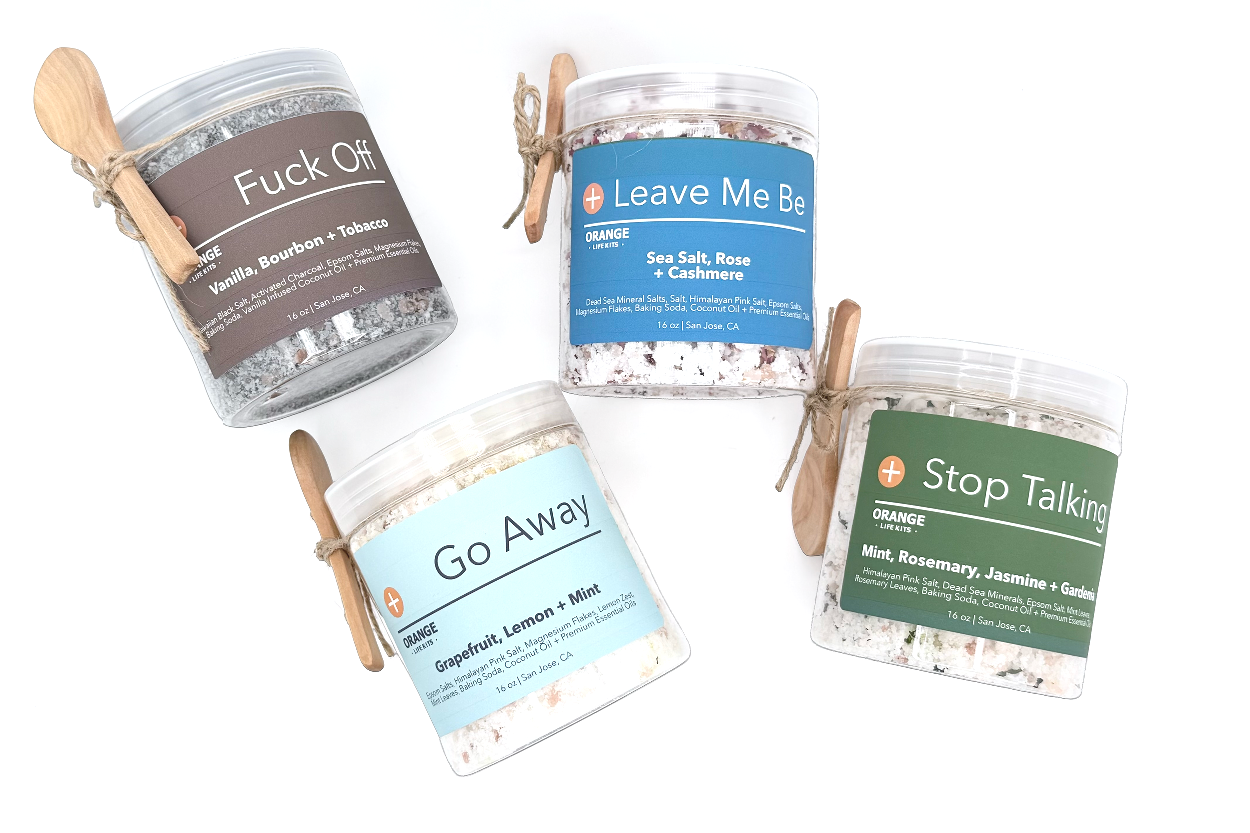 Several clear plastic jars with colorful labels, each containing bath salts. The labels have humorous and motivational messages such as "F*** Off," "Leave Me Be," "Go Away," and "Stop Talking." The jars are accessorized with small wooden spoons attached with twine.