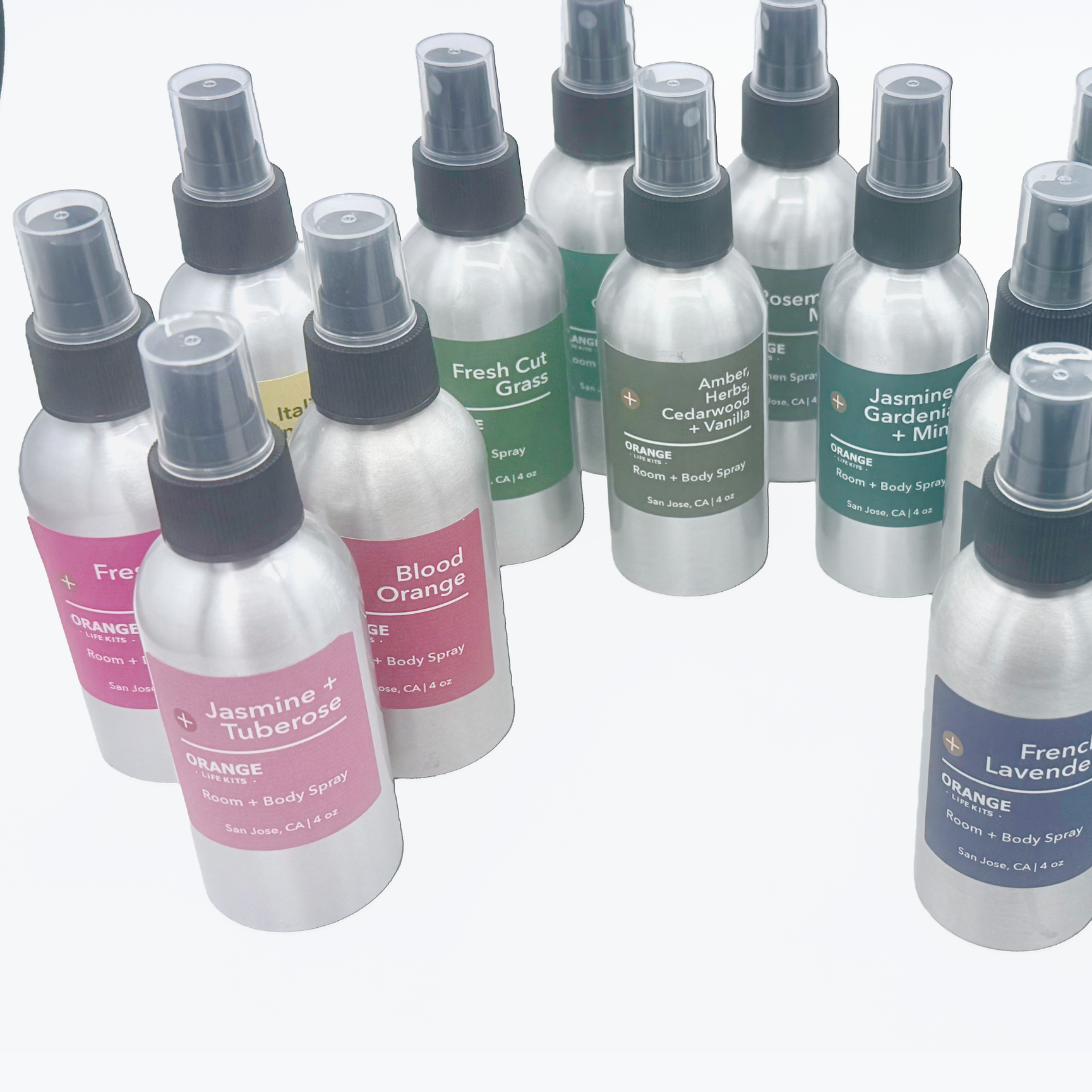 A collection of small spray bottles with labeled scents such as Fresh Cut Grass, Amber Herbs Cedarwood Vanilla, Jasmine Gardenia Mint, Blood Orange, and French Lavender, arranged on a white surface.