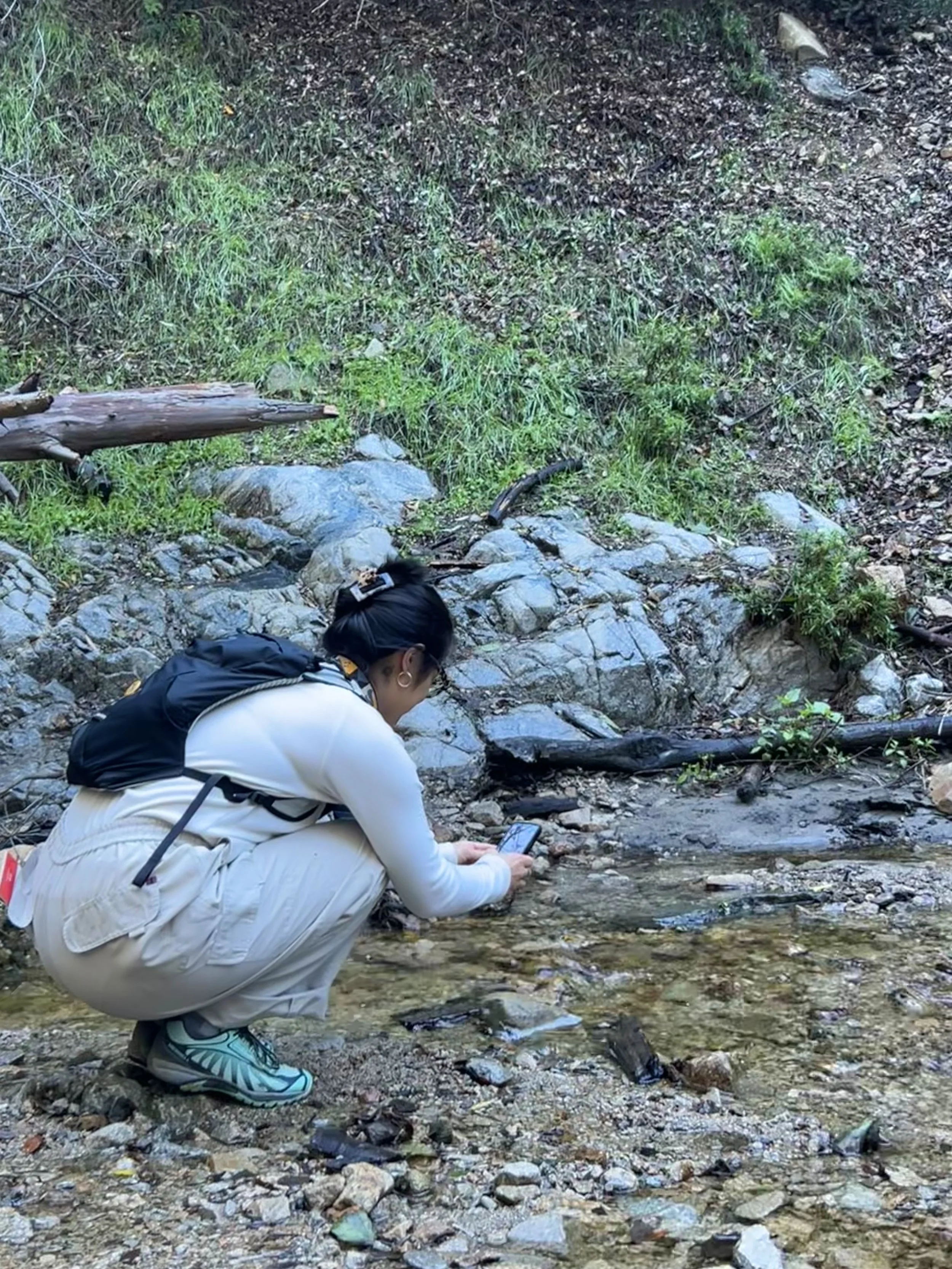 Amanda crouching down taking a video of a creek in the Angeles National Forest