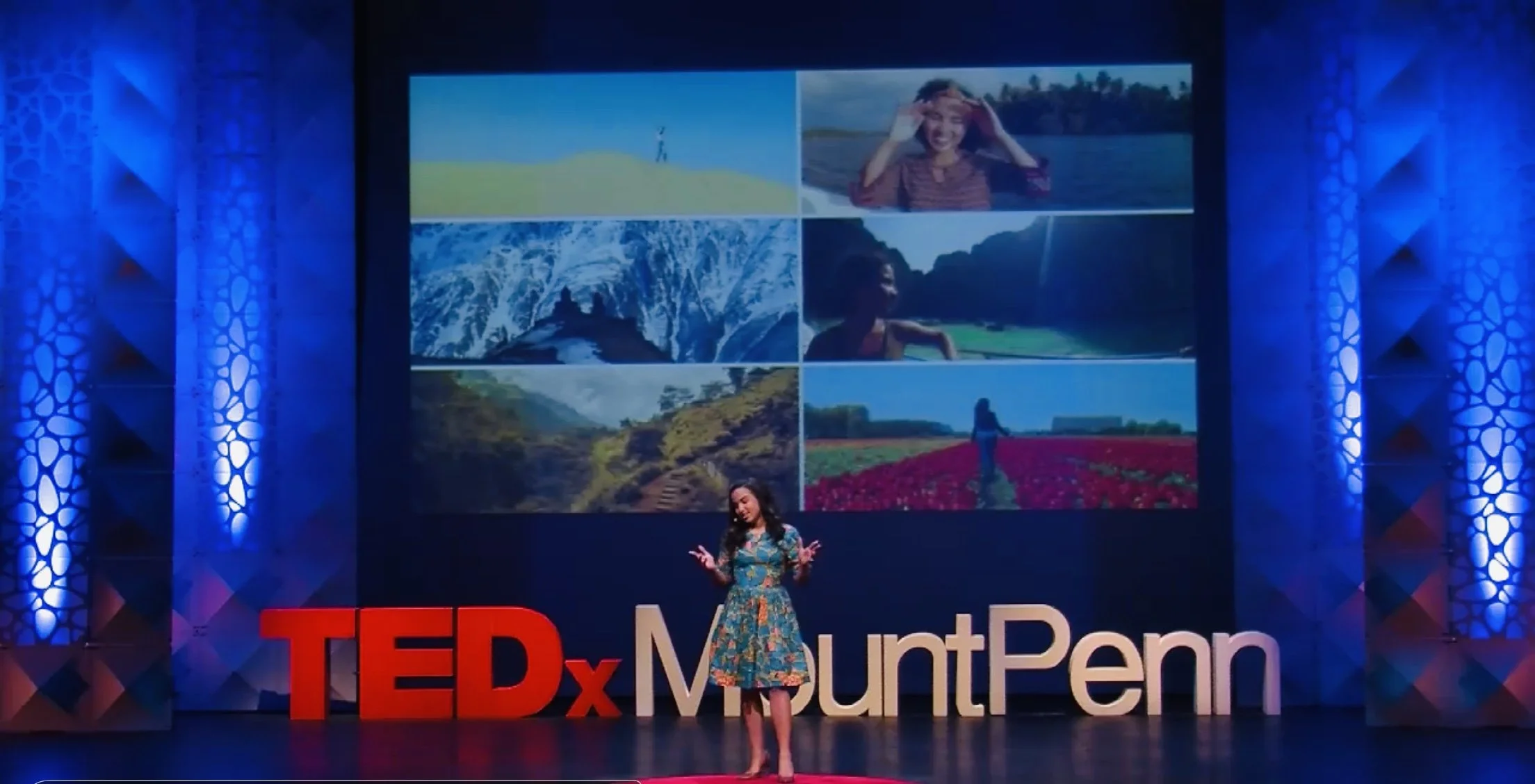 A woman in a colorful dress stands on stage at a TEDx event at Mount Penn, with a large screen behind her displaying six outdoor nature photographs and the TEDx Mount Penn logo.