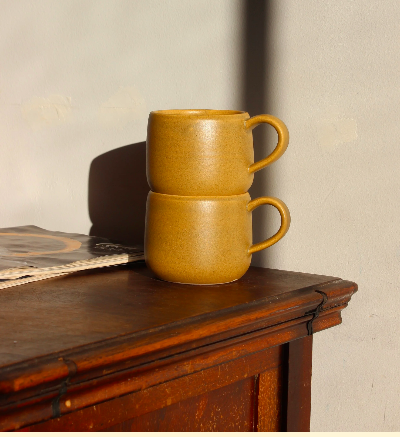 Andrea D'Angelo Ceramics.  A ceramic artist in Victoria, BC.  Two stacked ceramic mugs on a wooden surface next to a book, with sunlight and shadow in the background.