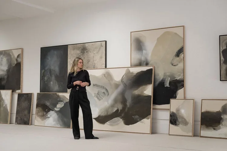 Joy Kinna, a painter and artist in Victoria, BC. A woman in black pants and a black top stands in an art gallery surrounded by large abstract black, white, and gray paintings leaning against the wall.