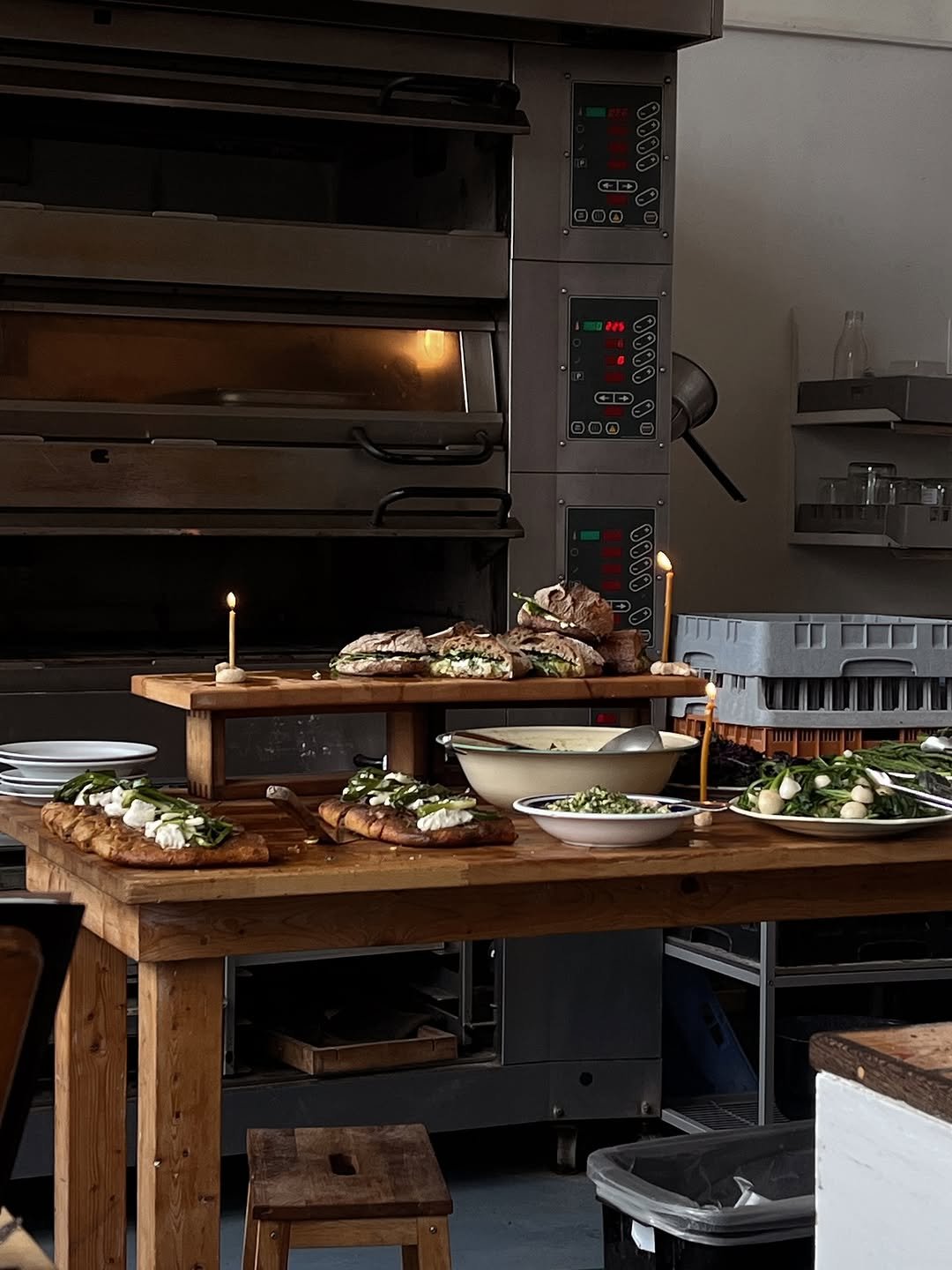 A woman taking a selfie from above, smiling with her eyes closed, wearing a large hat, multiple rings on her fingers, and a patterned pink top. The background shows a room with furniture and a cow print rug.