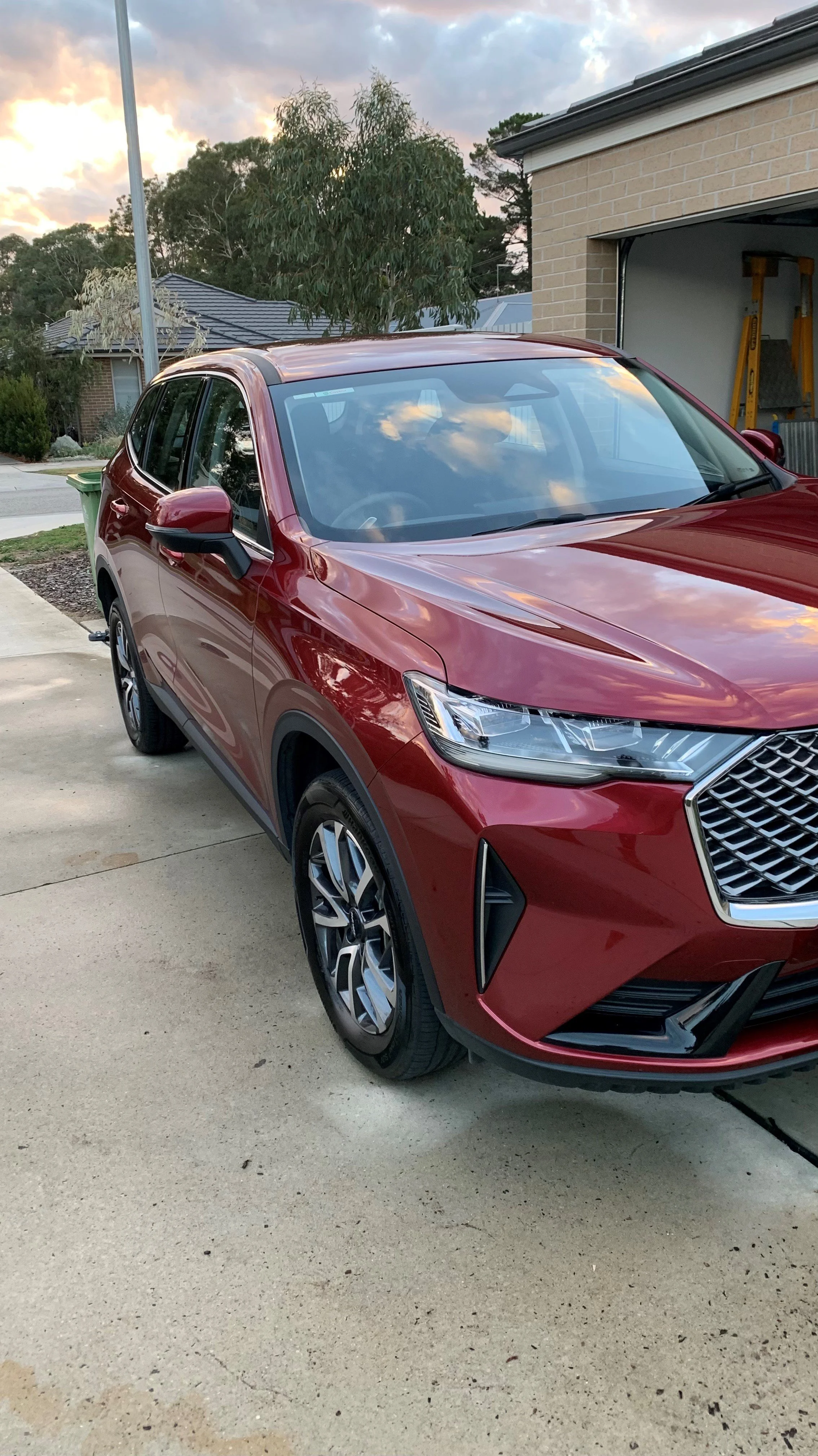 Red SUV parked on driveway in front of a garage during sunset.