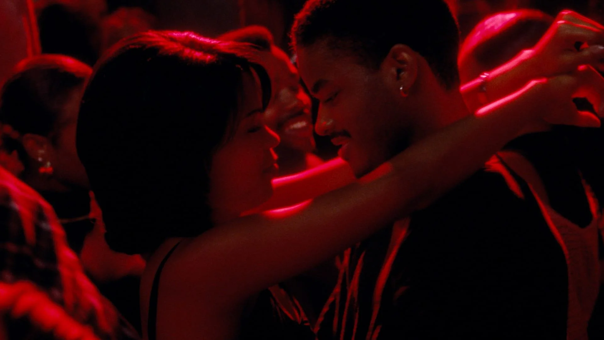 Cena do filme Love Jones. Na imagem temos a imagem de Nina (Nia Long), uma mulher negra, de cabelo curto preto liso. Ao seu lado está Darius (Larenz Tate), homem negro, cabelo preto raspado. Eles estão em uma festa, com luzes vermelhas e pretas.