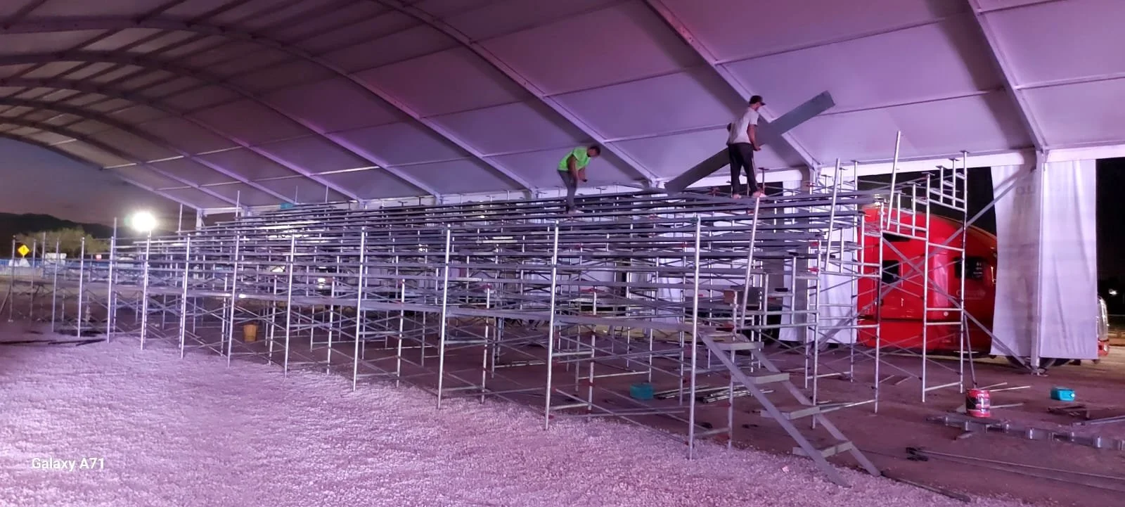 Personas armando gradas metálicas en un espacio cubierto con iluminación color púrpura en la noche.
