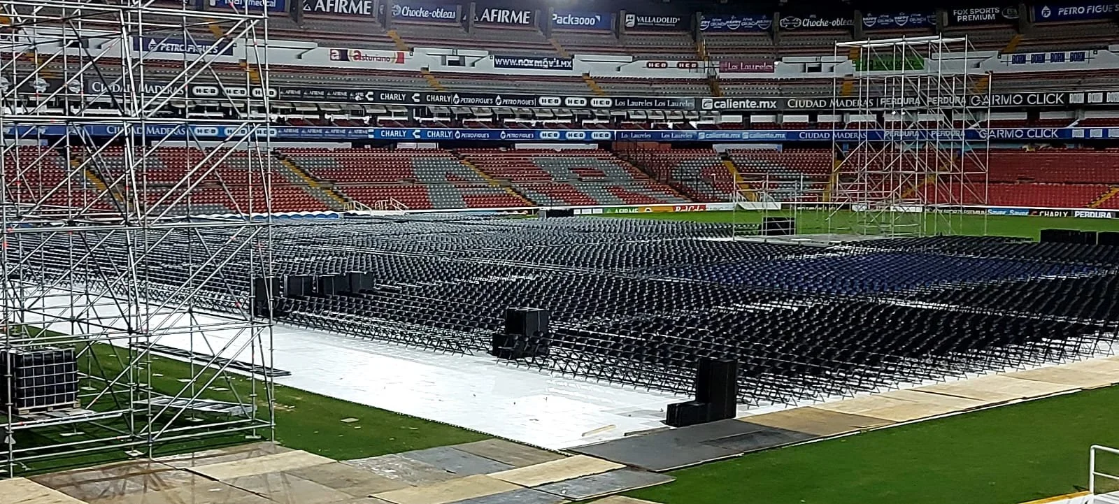 Estructuras de palcos y asientos vacíos en un estadio para un evento, con gradas y anuncios publicitarios en el fondo.