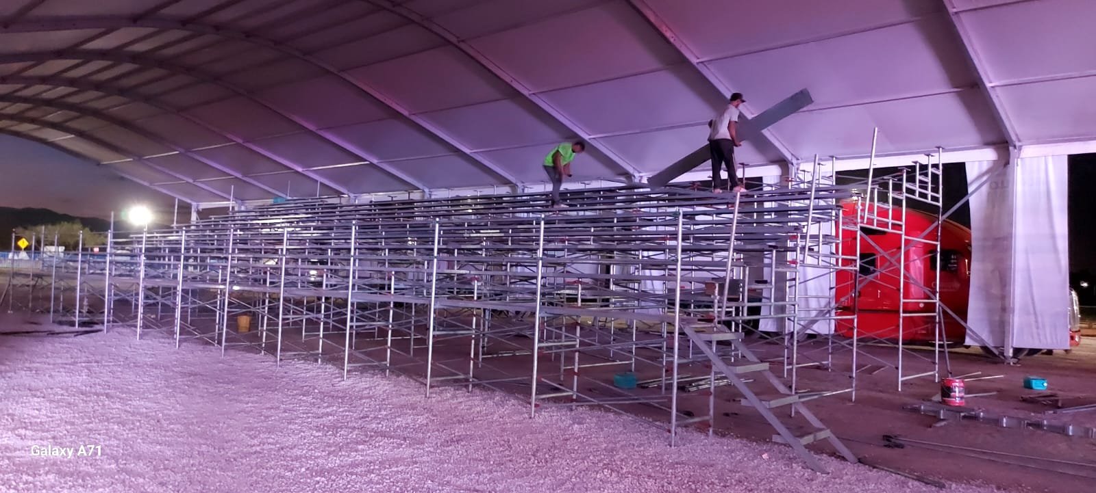 Personas instalando gradas metálicas en un espacio techado, trabajando con equipos y estructuras de soporte.