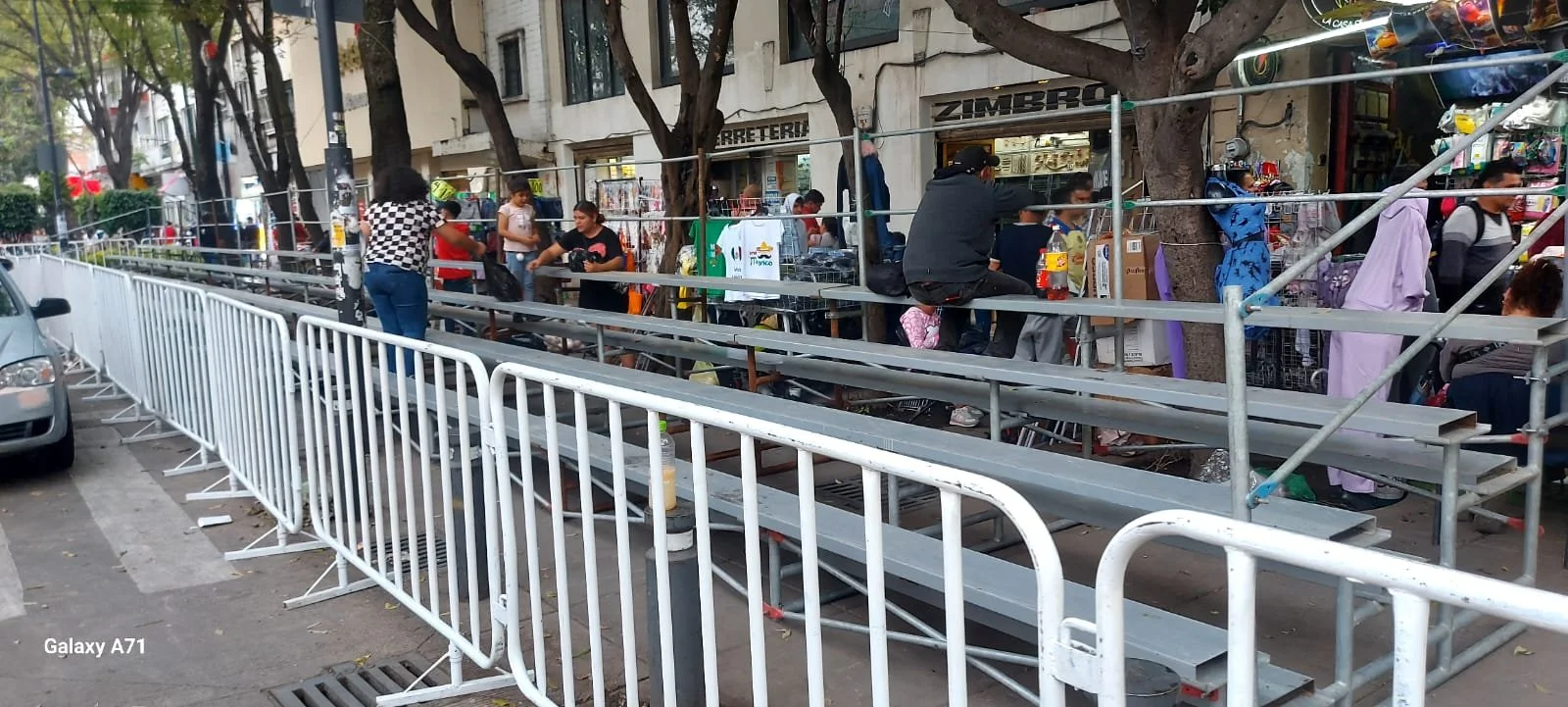 Había una estructura de gradas de metal en una acera, con varias personas alrededor y algunos tomando fotos, y una tienda con artículos, en la ciudad.