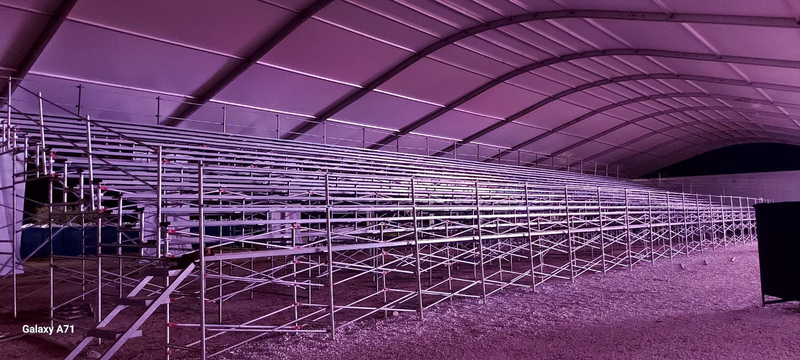 Estructura metálica y andamios en un espacio cubierto con iluminación morada.