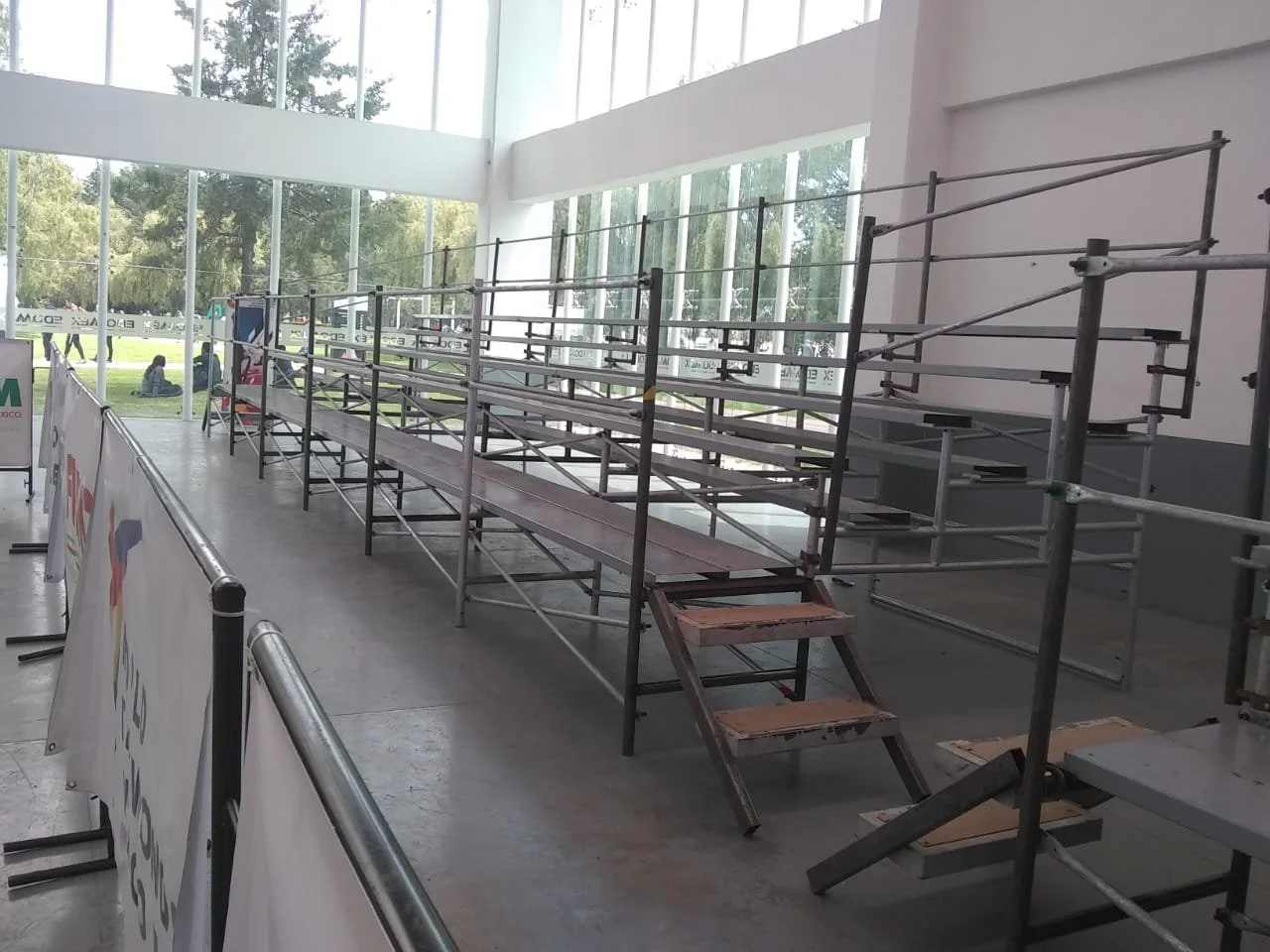 Estructuras de andamios vacías en interior con ventanas grandes y vistas de árboles en el exterior.