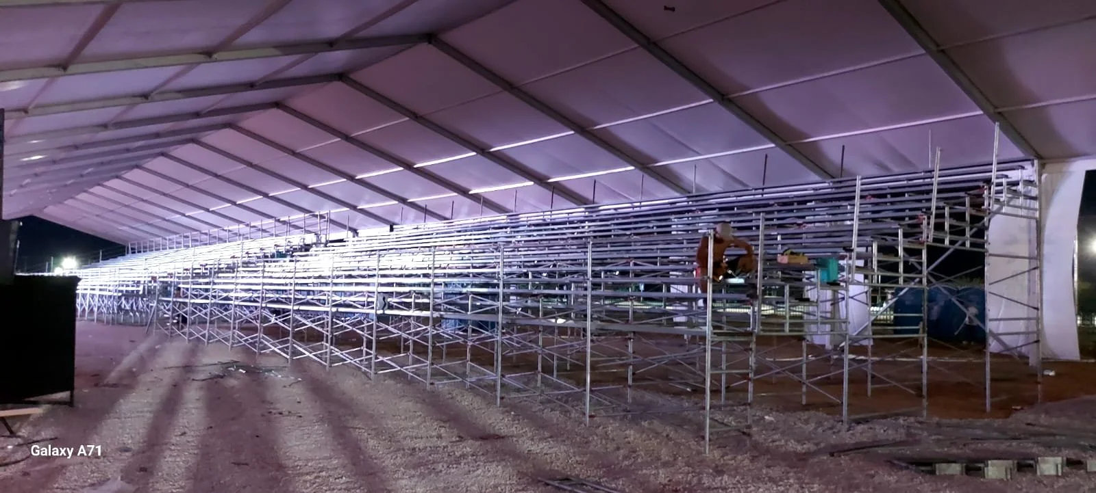 Estructura metálica en construcción bajo una cubierta de telón, con personas trabajando en la estructura y luces instaladas.