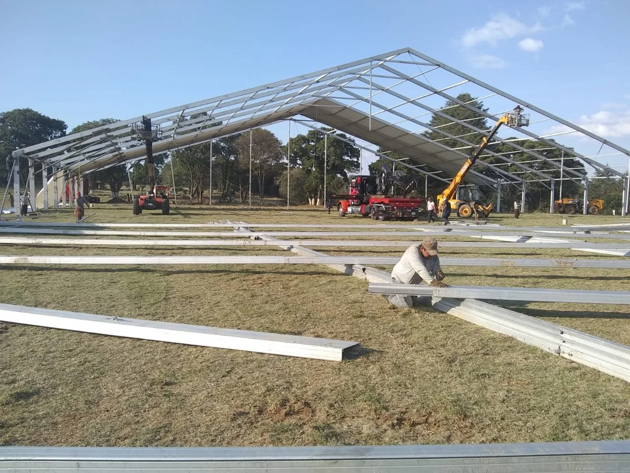 Construcción de una estructura metálica grande en un campo, con varias máquinas y trabajadores ensamblando los componentes de la estructura.