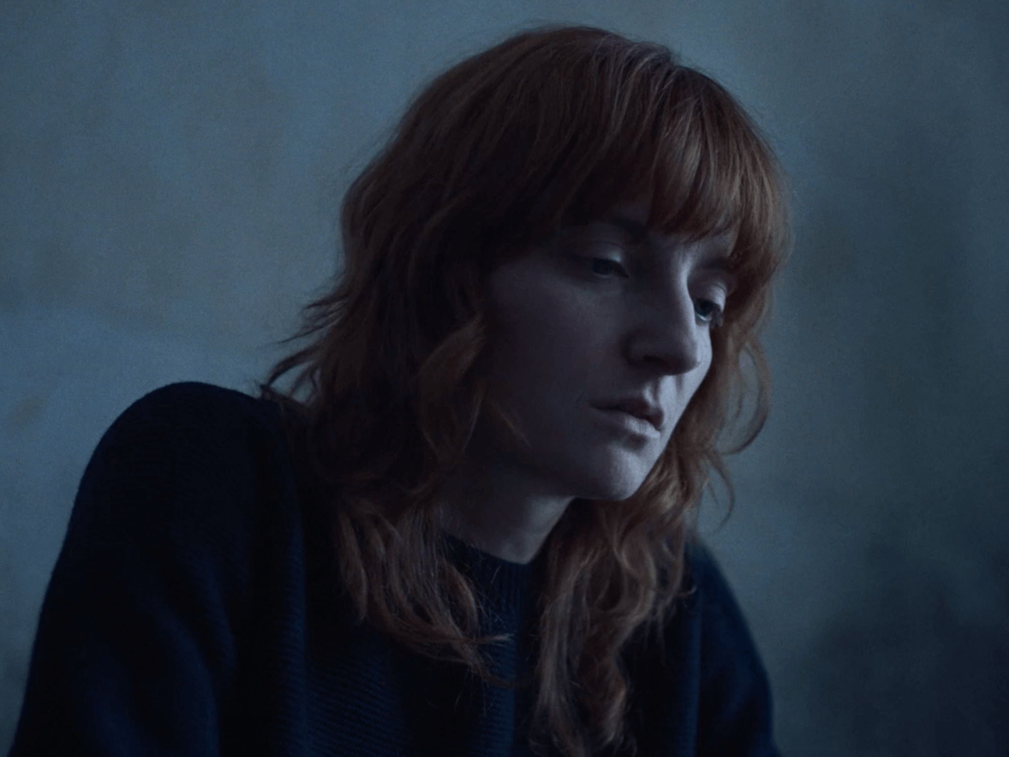 une femme aux cheveux roux regarde vers le bas dans un environnement sombre et calme